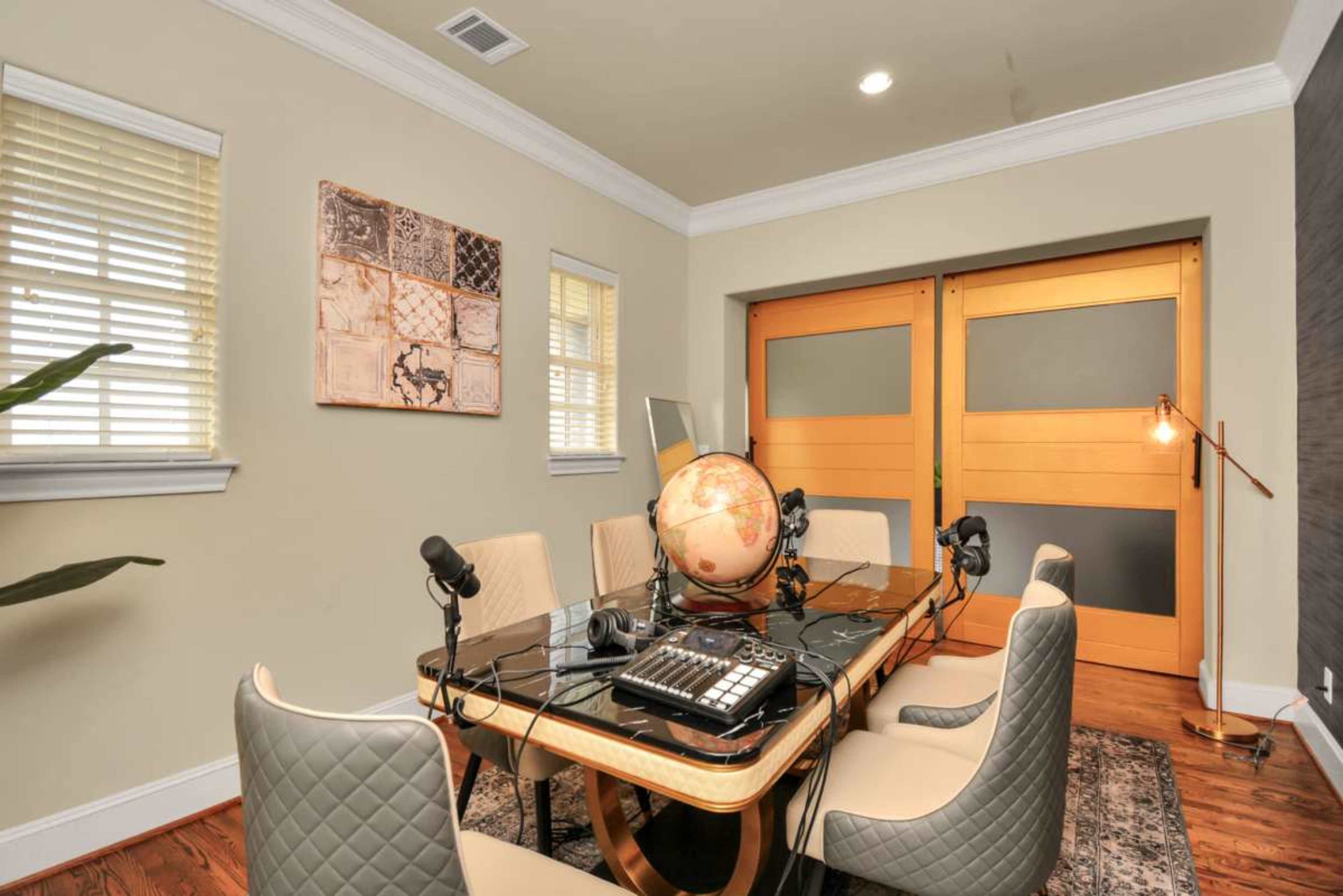 The image shows a modern conference room featuring a round table with microphones, a globe, and sliding wooden doors.
