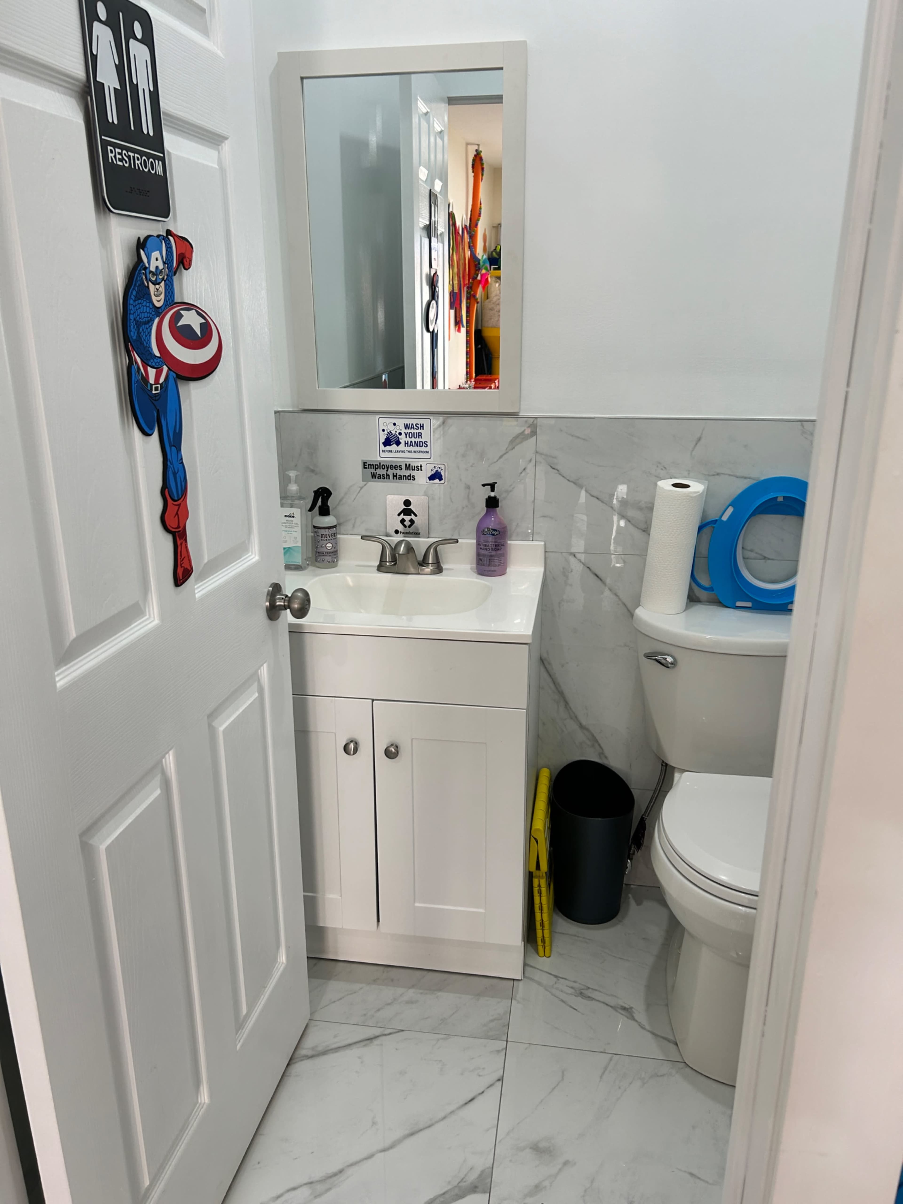 A small bathroom with a sink, toilet, mirror, and various hygiene products on a white marble countertop.