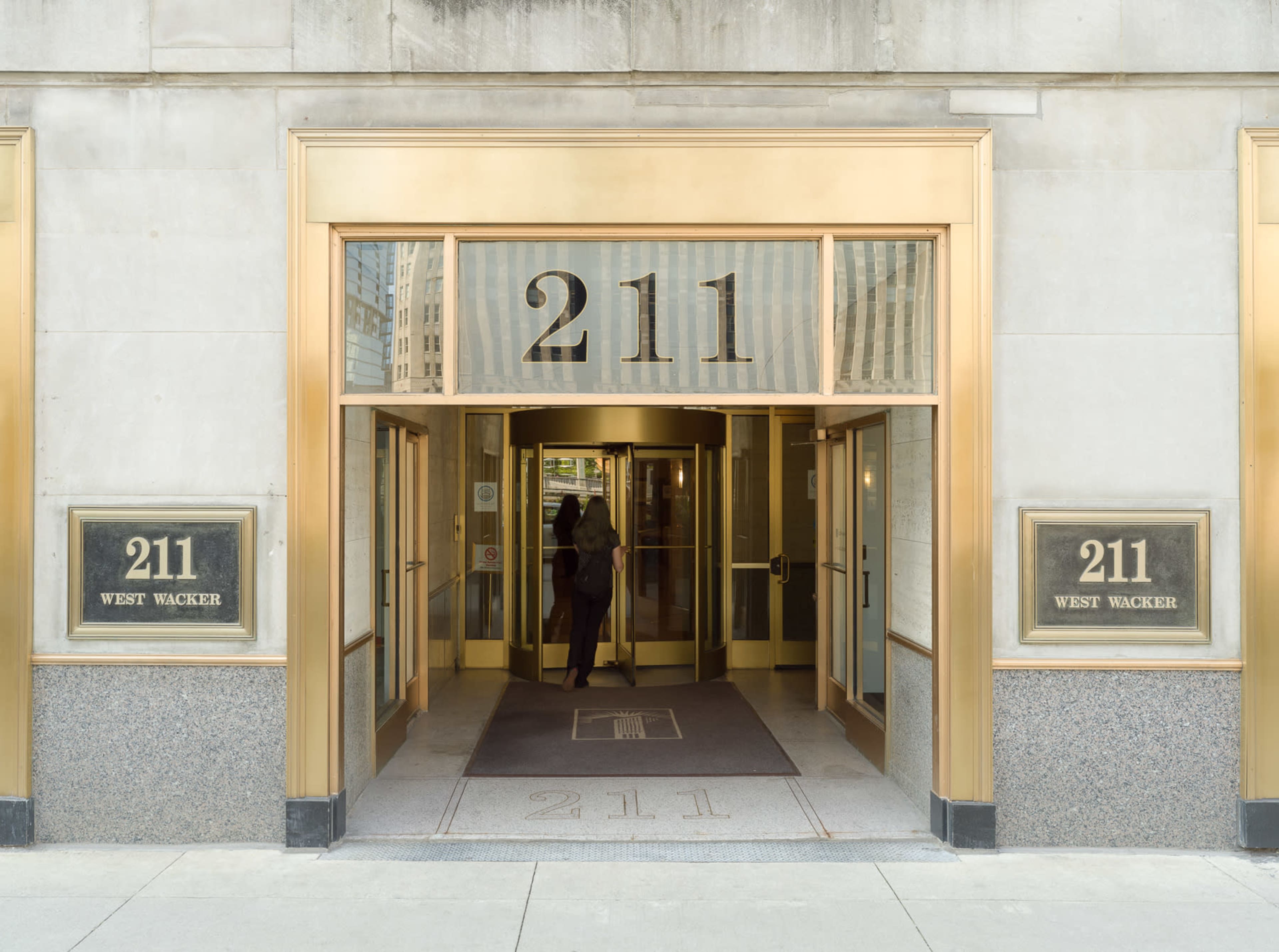 The entrance of a building at 211 West Wacker is framed by large glass doors and gold accents, featuring the building number prominently displayed.