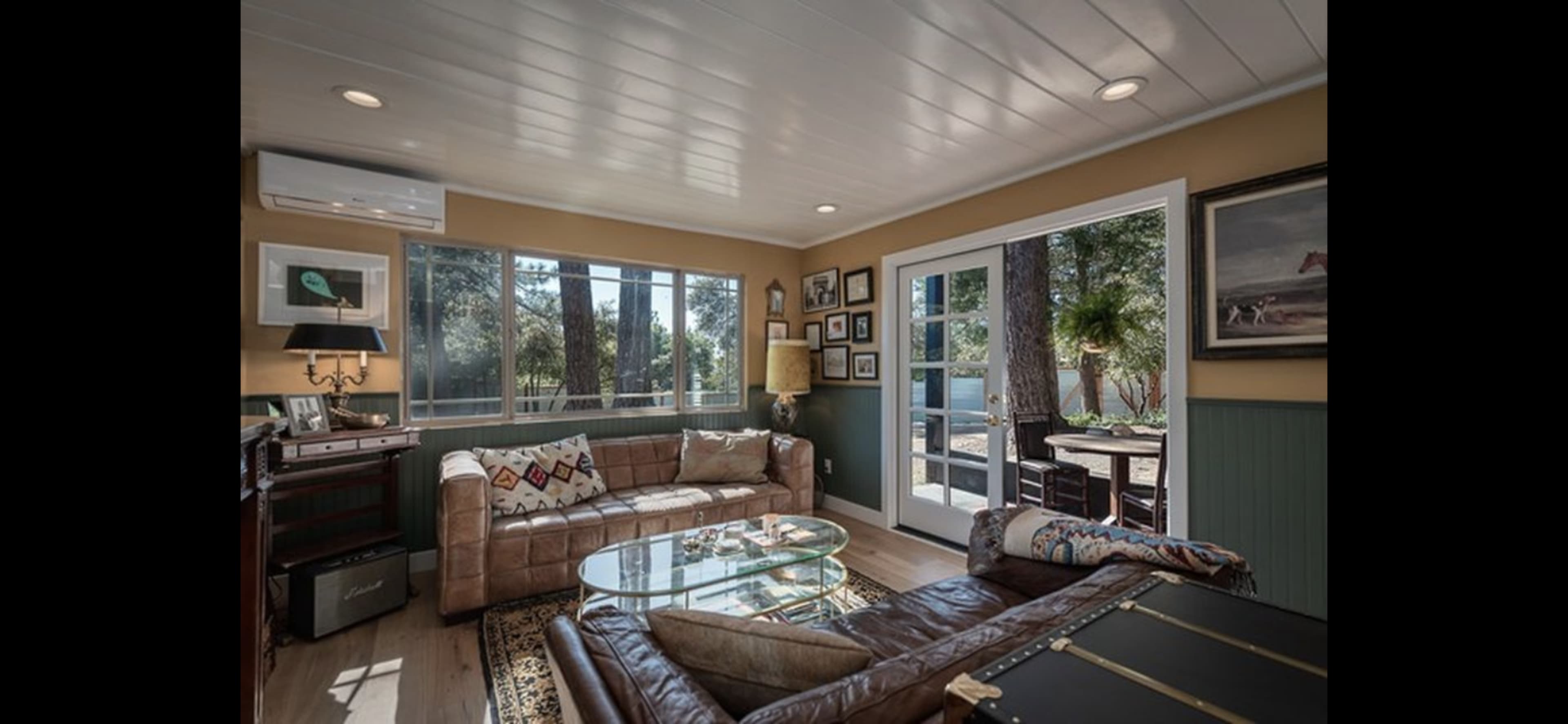 A cozy living room with a leather sofa, a glass coffee table, and large windows overlooking a garden.