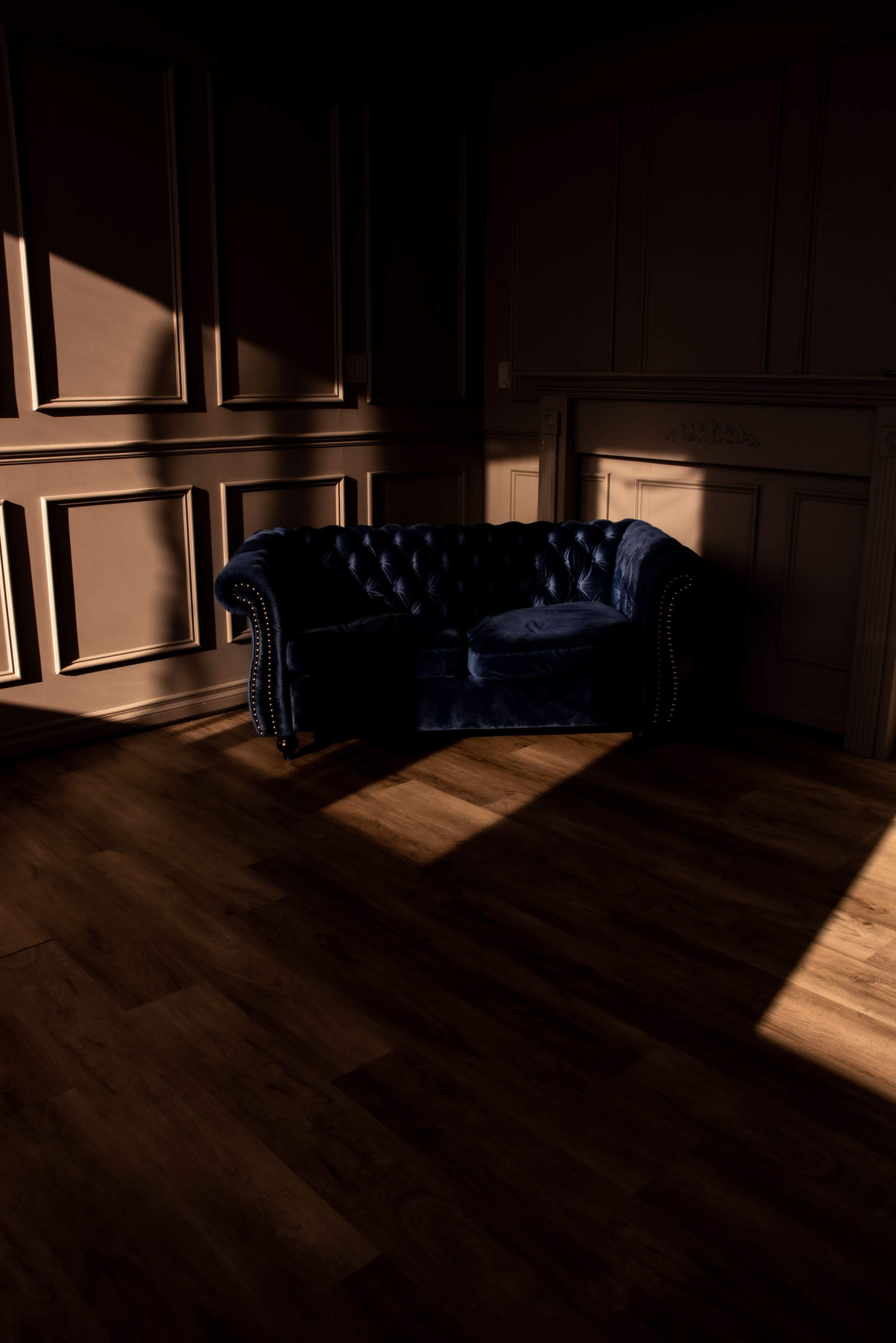 A dark room features a blue upholstered couch partially illuminated by sunlight.