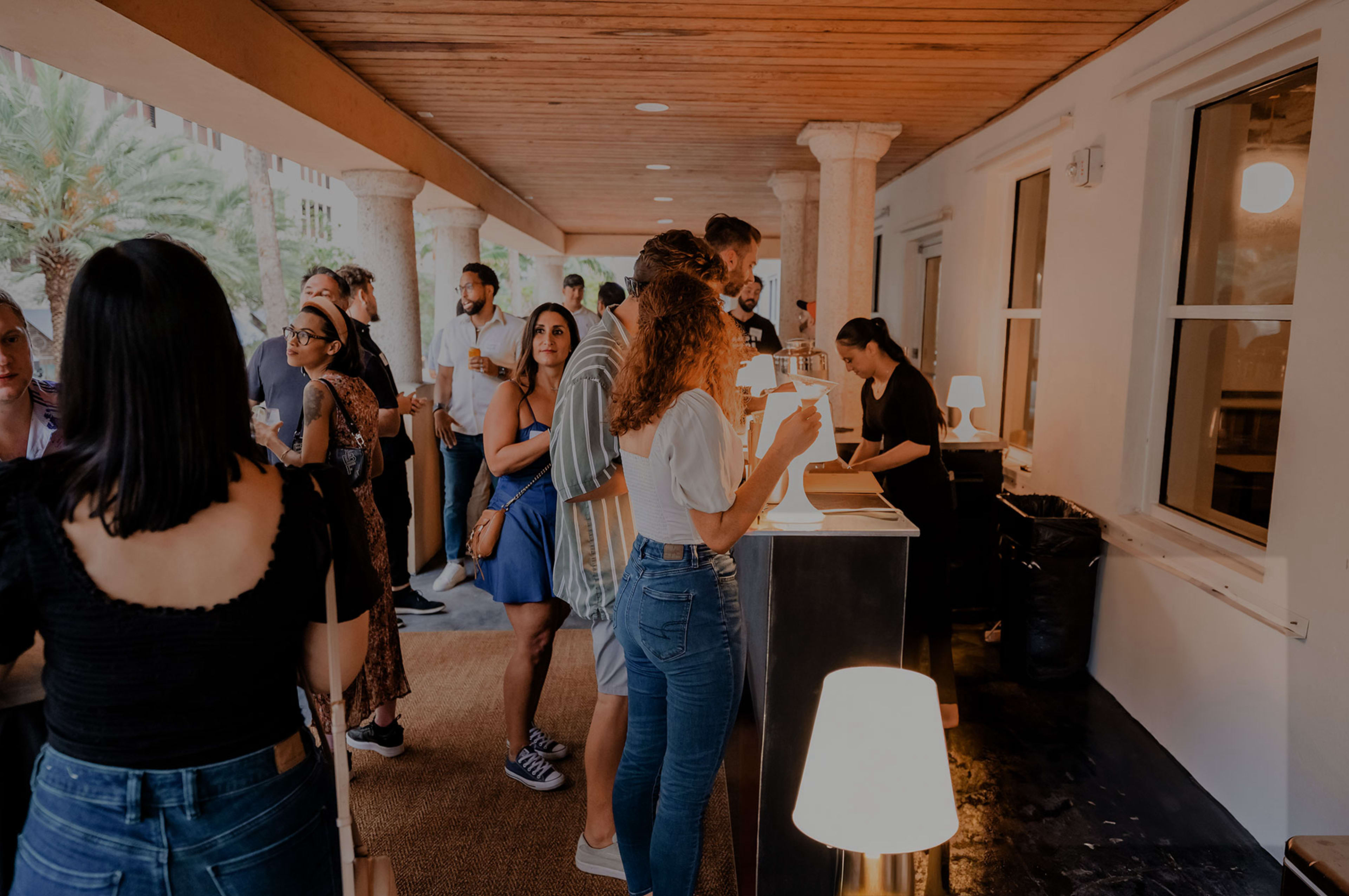 People are gathered at a counter in a well-lit corridor, engaging in conversations and ordering refreshments.