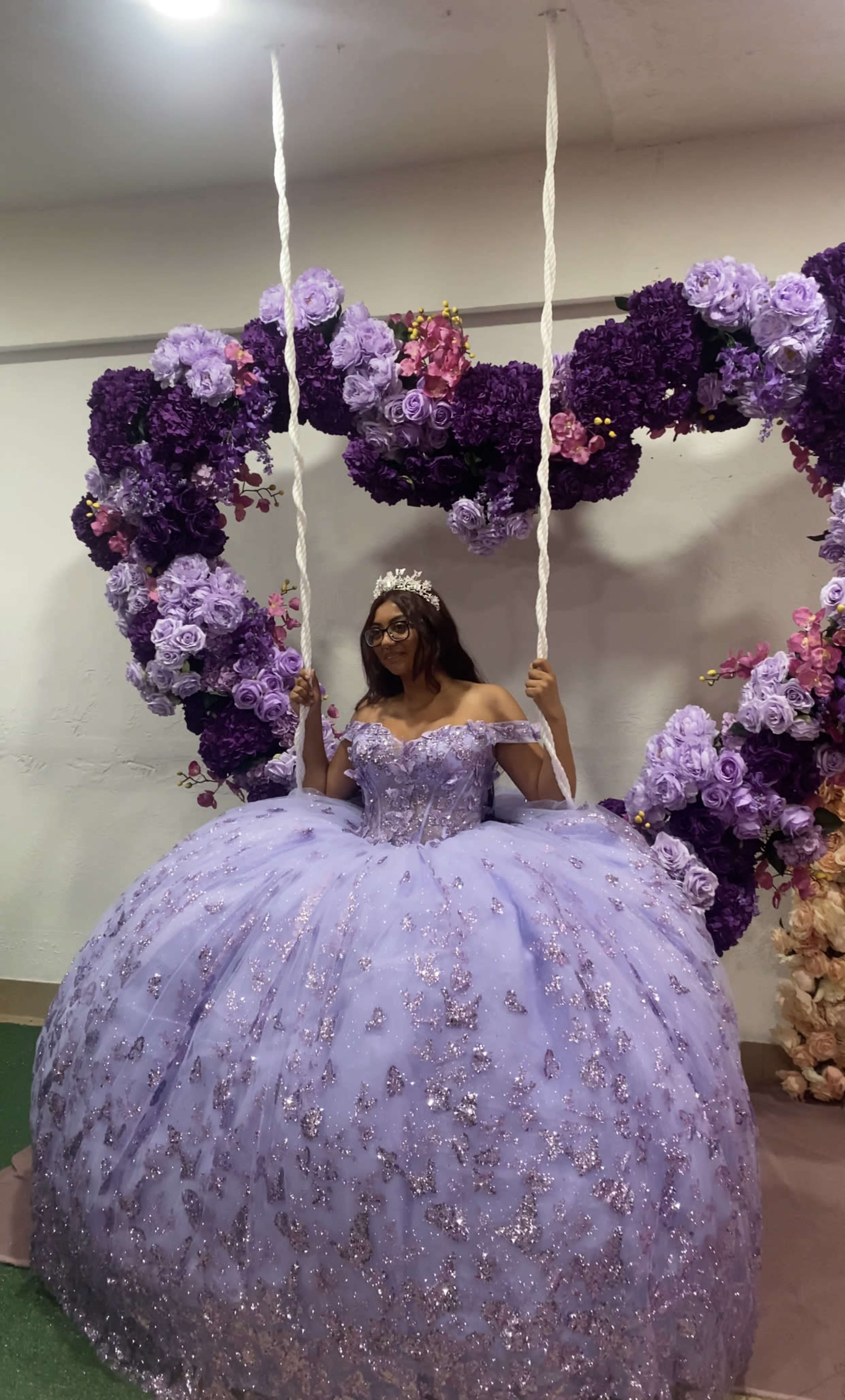 A person wearing a lilac gown is sitting on a swing adorned with purple and pink floral decorations.