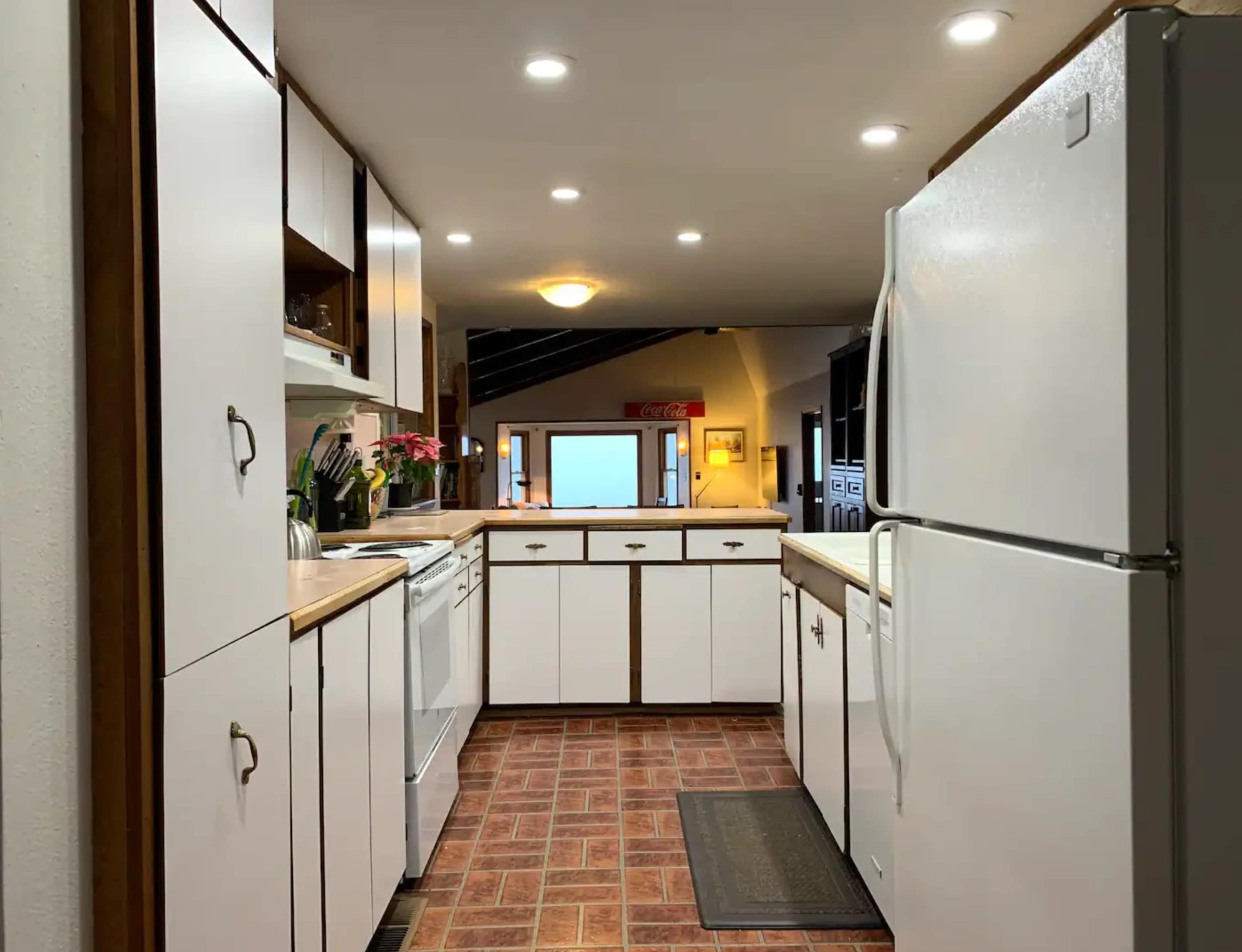 A modern kitchen with white cabinets, a refrigerator, and a view toward an external window.