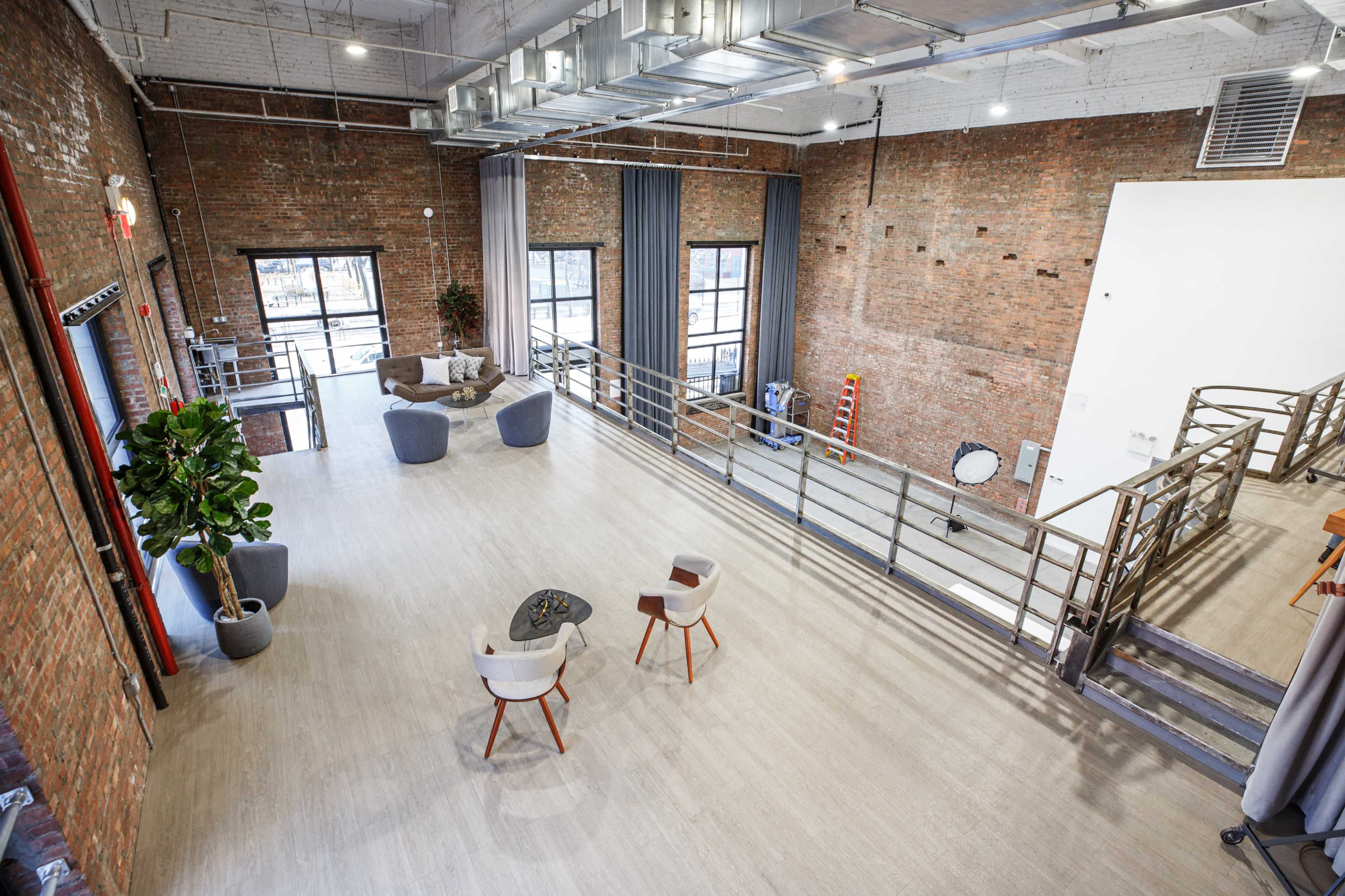 A spacious industrial-style room with exposed brick walls, large windows, and a modern seating area.