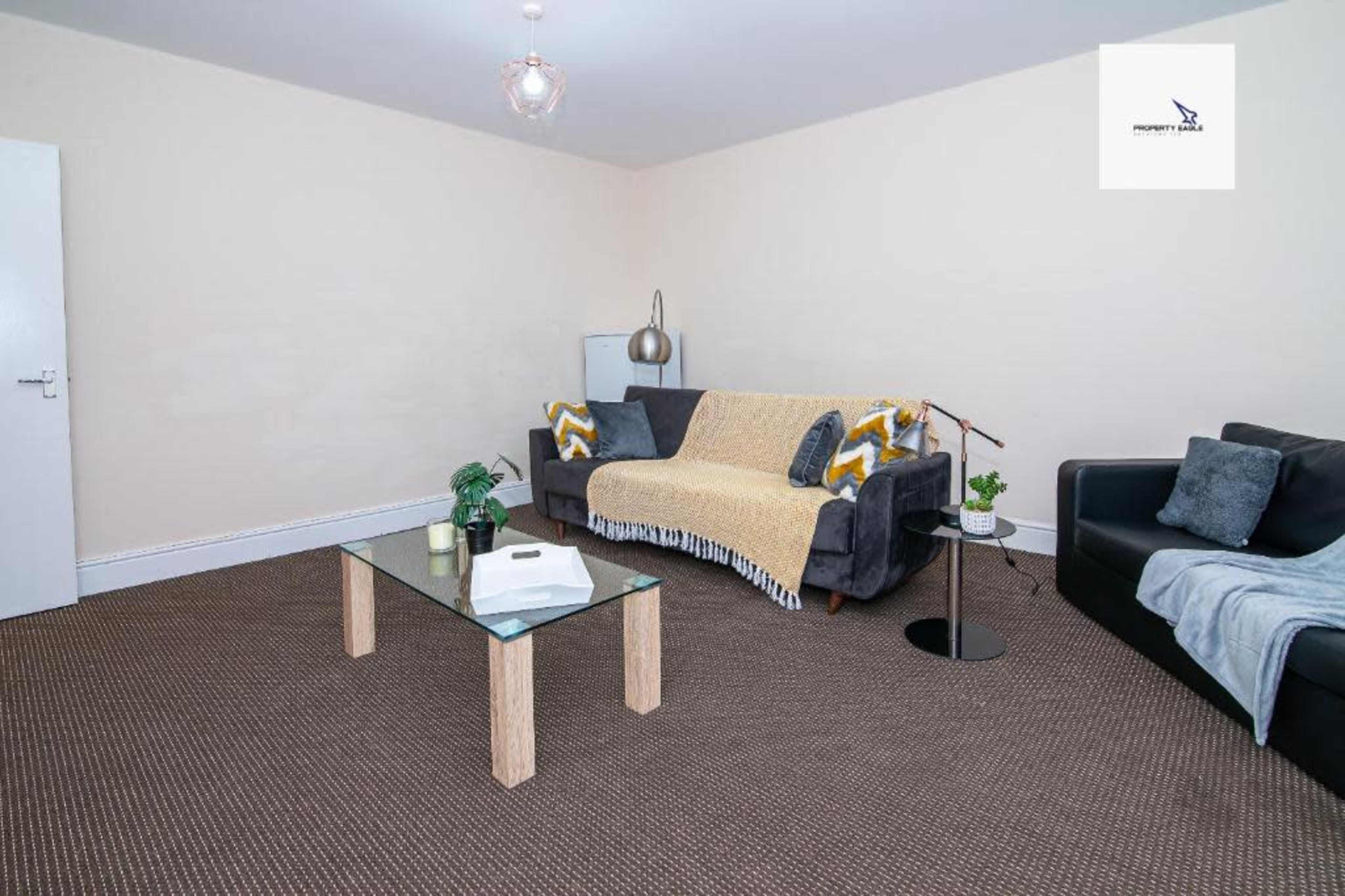 A living room with two couches, a glass coffee table, and a corner plant on a carpeted floor.