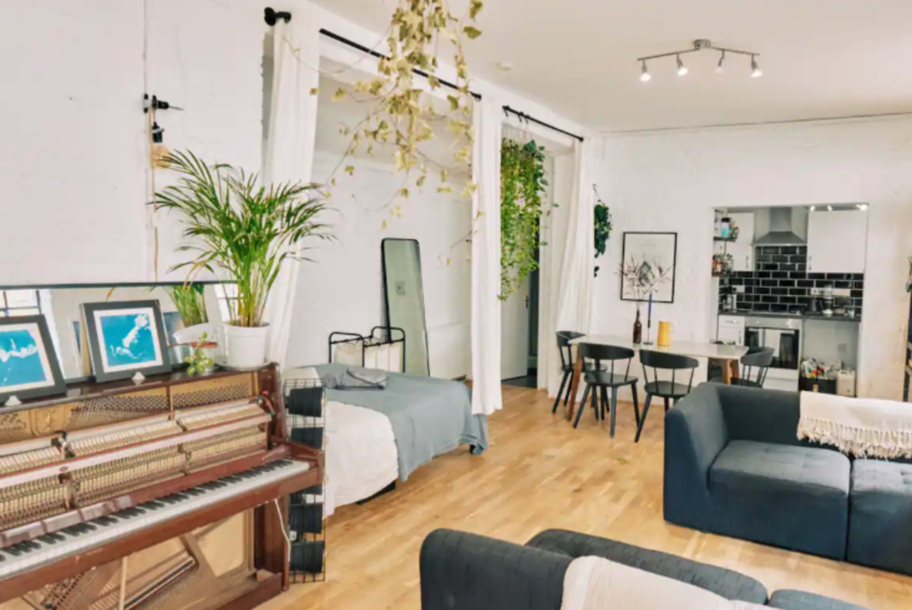 A bright, open living space featuring a piano, a bed, a dining area, and a kitchen with modern appliances.