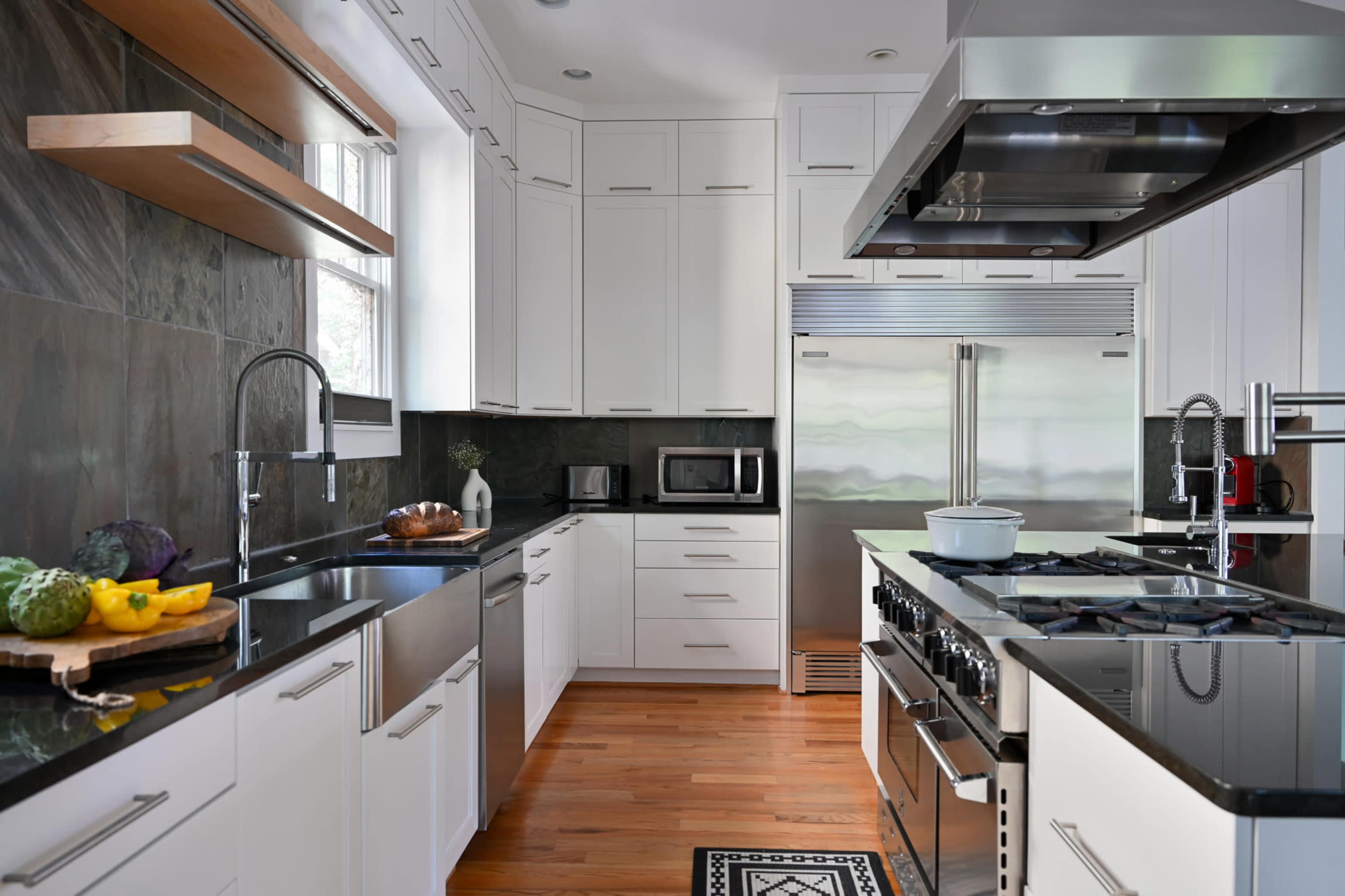 A modern kitchen features white cabinetry, stainless steel appliances, and a dark stone backsplash with wooden shelves.