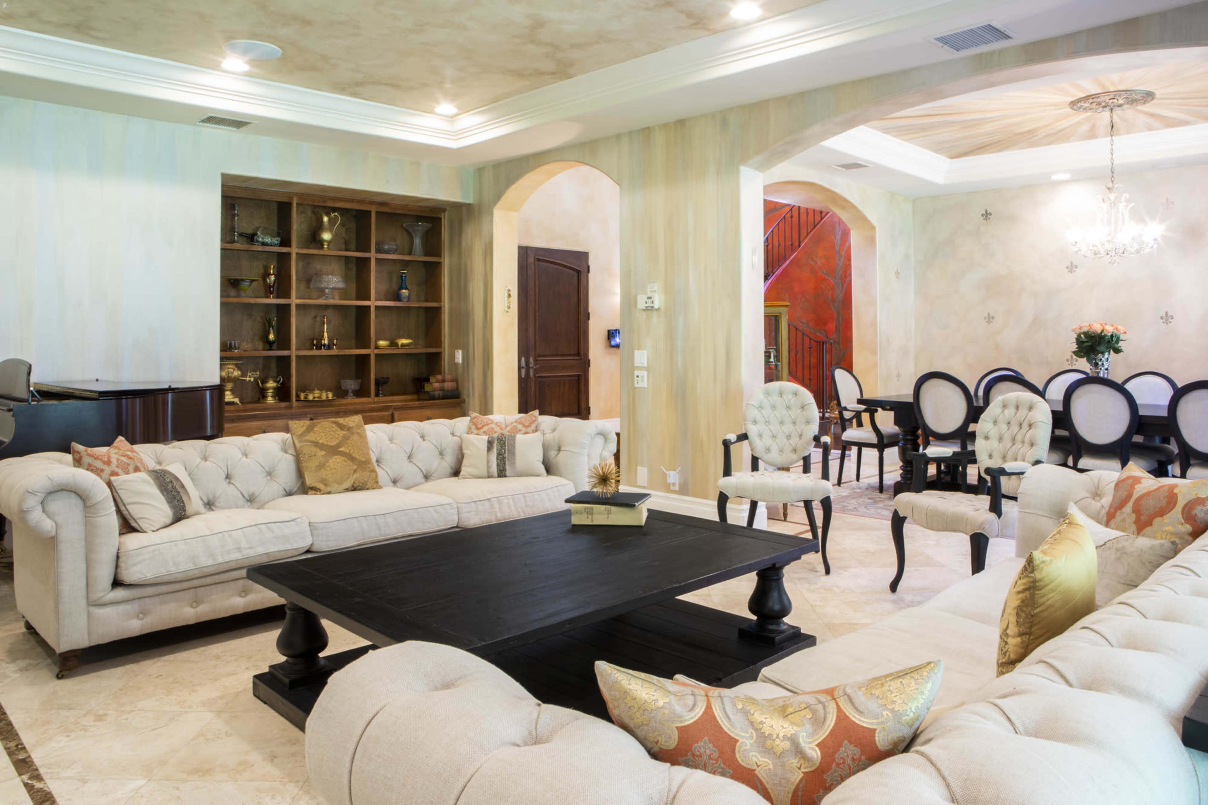 A spacious living area featuring a large, upholstered sofa set arranged around a dark coffee table, with a dining area visible in the background.