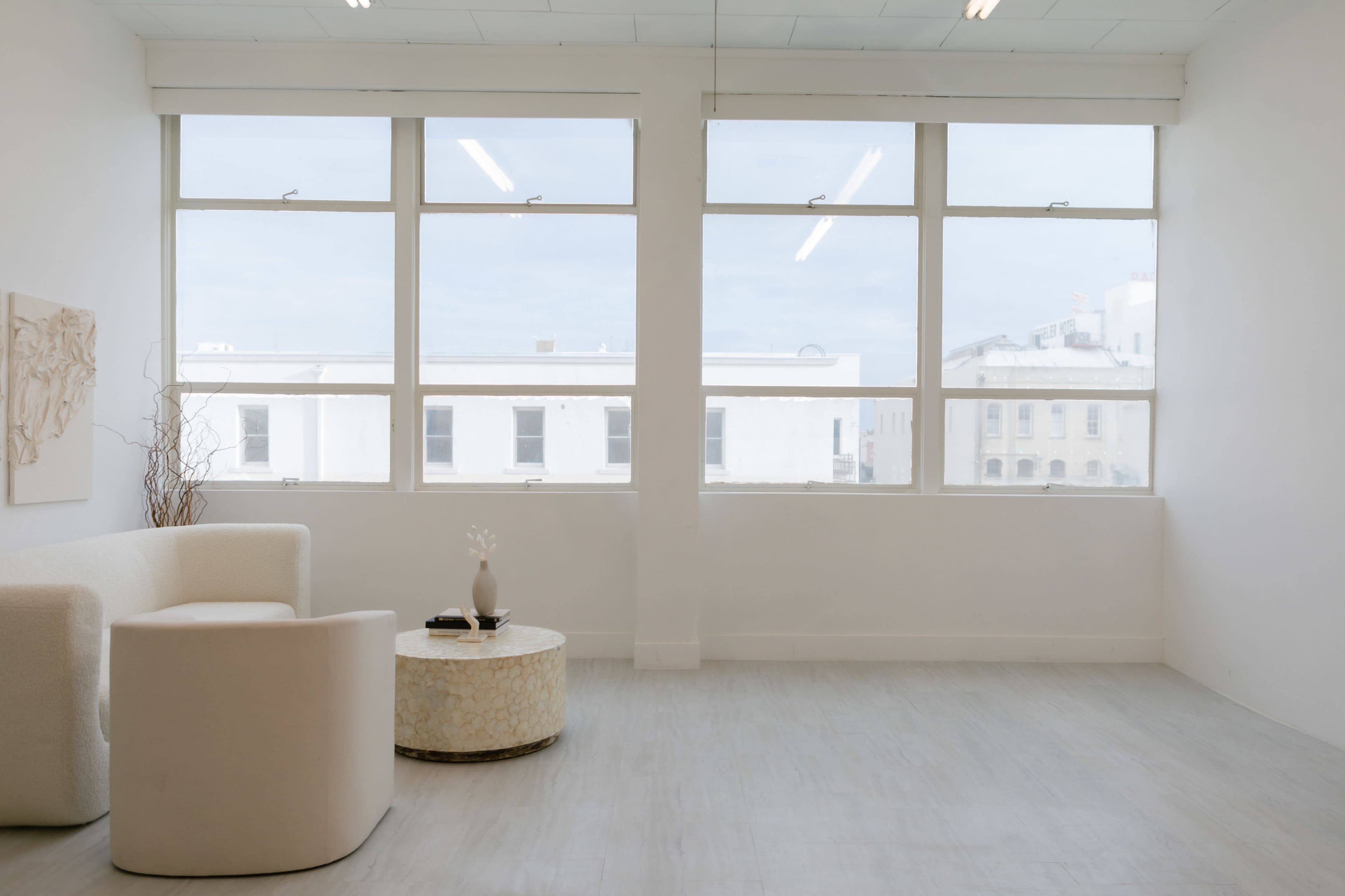 The image shows a minimalist interior space featuring large windows, a white sofa, and a round coffee table.