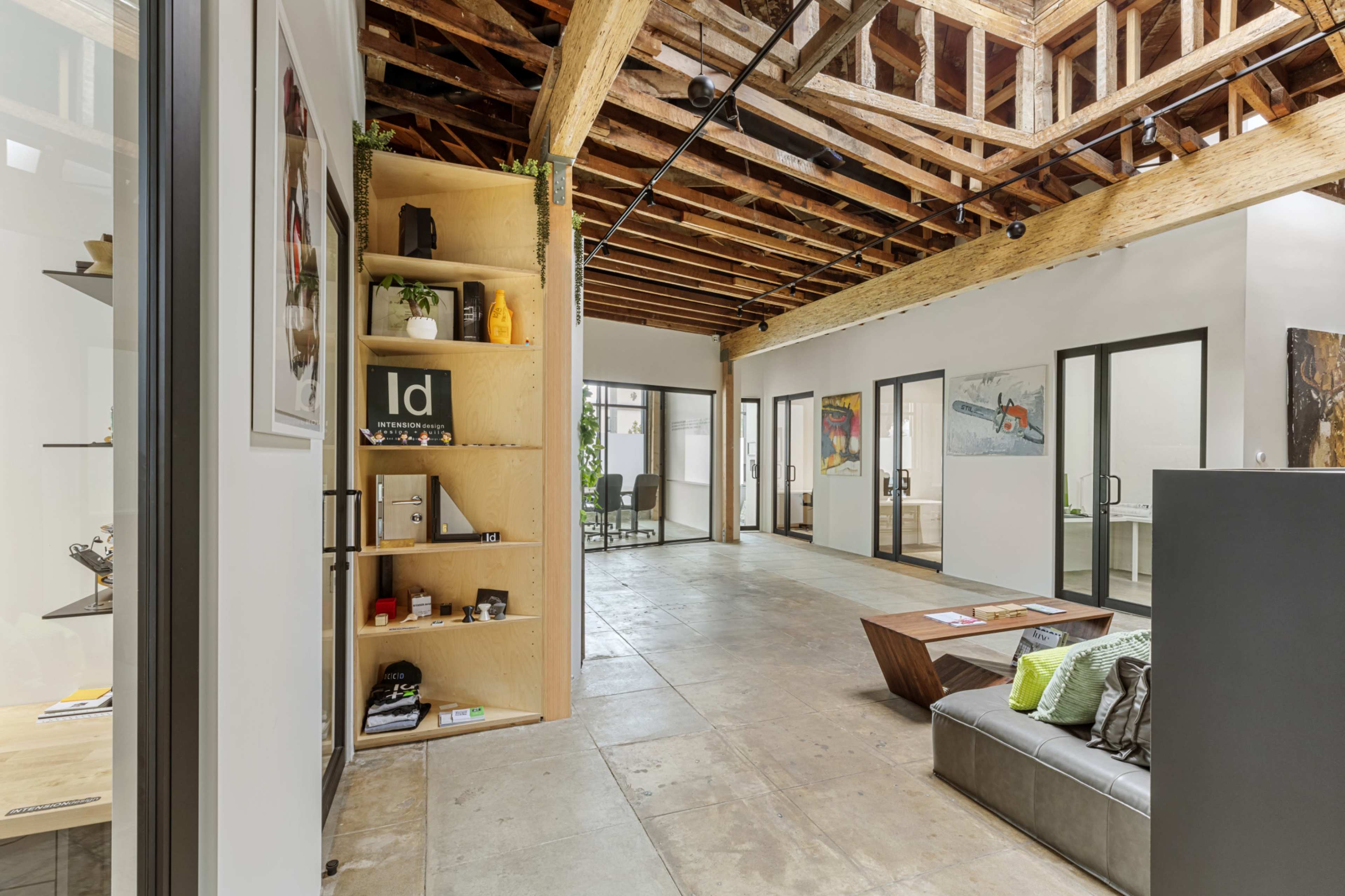 The image shows an open office space with a high wooden ceiling, modern furniture, and glass-walled meeting rooms.