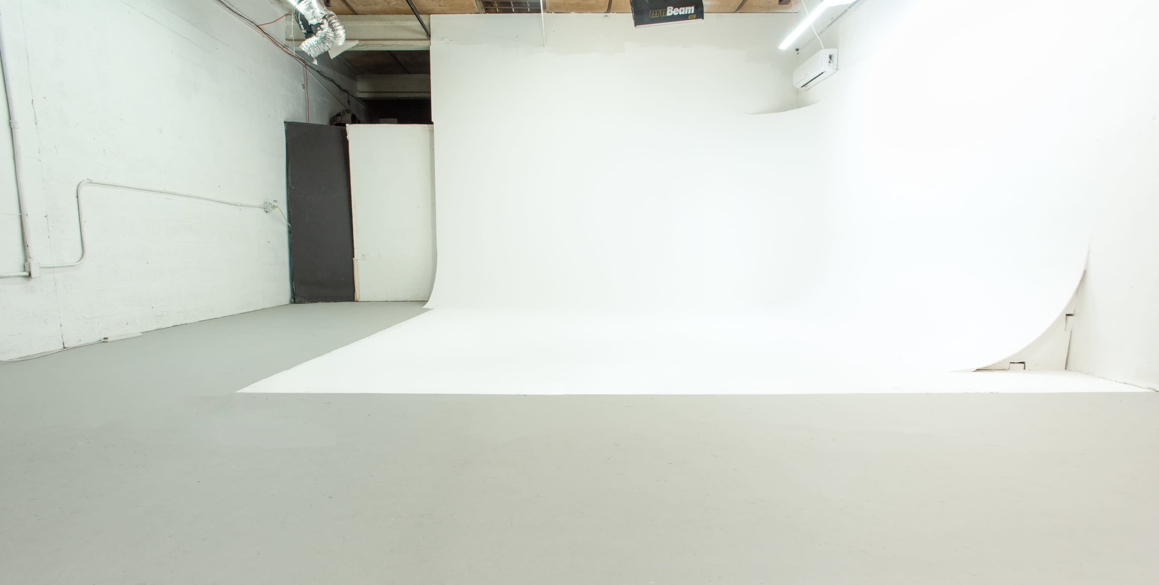An empty studio space features a seamless white backdrop, gray flooring, and a few scattered light fixtures.