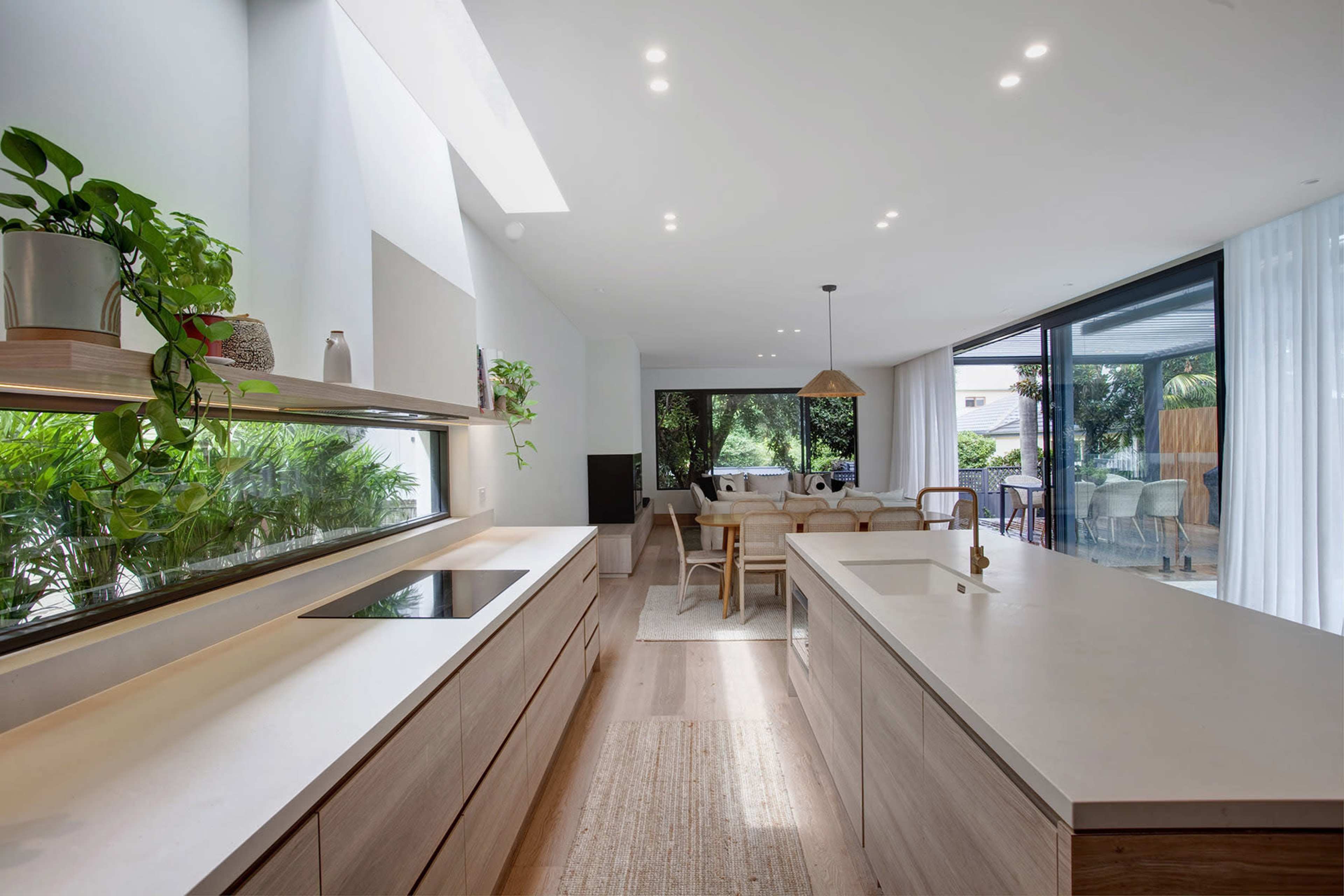 A contemporary kitchen with wooden cabinetry and a large island, connected to a dining area featuring a table and chairs, all illuminated by natural light.