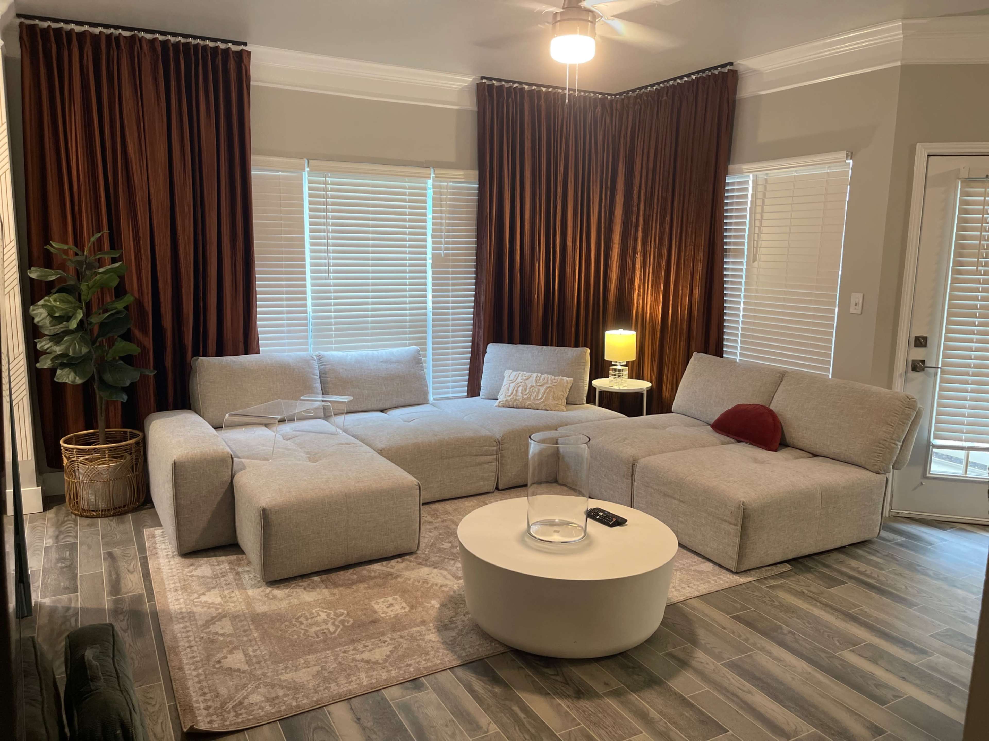 A modern living room featuring a large gray sectional sofa, a round white coffee table, and dark curtains, with a floor lamp beside the window.