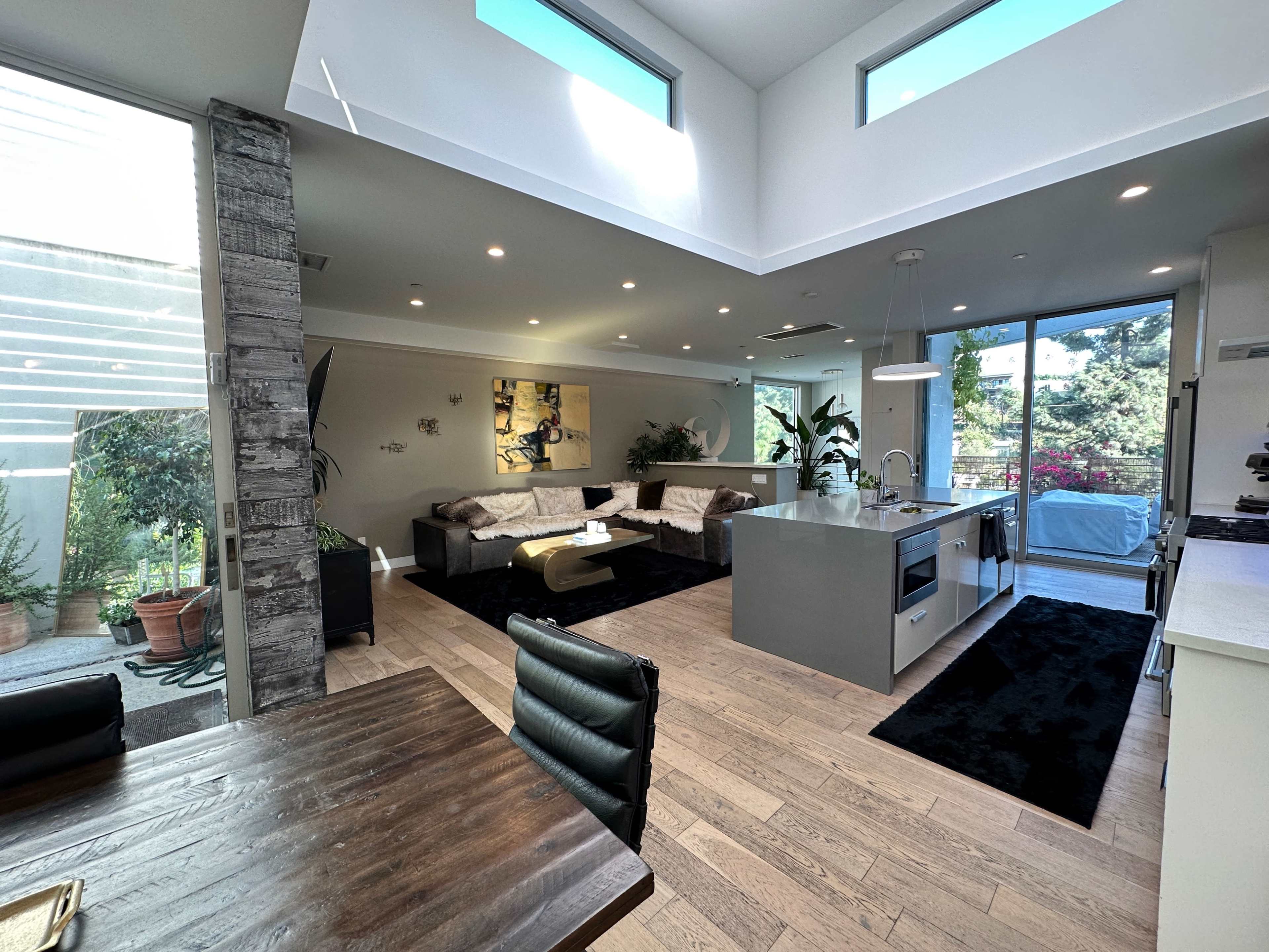 A modern, open-concept living space featuring a kitchen, dining area, and comfortable seating with large windows allowing natural light to enter.