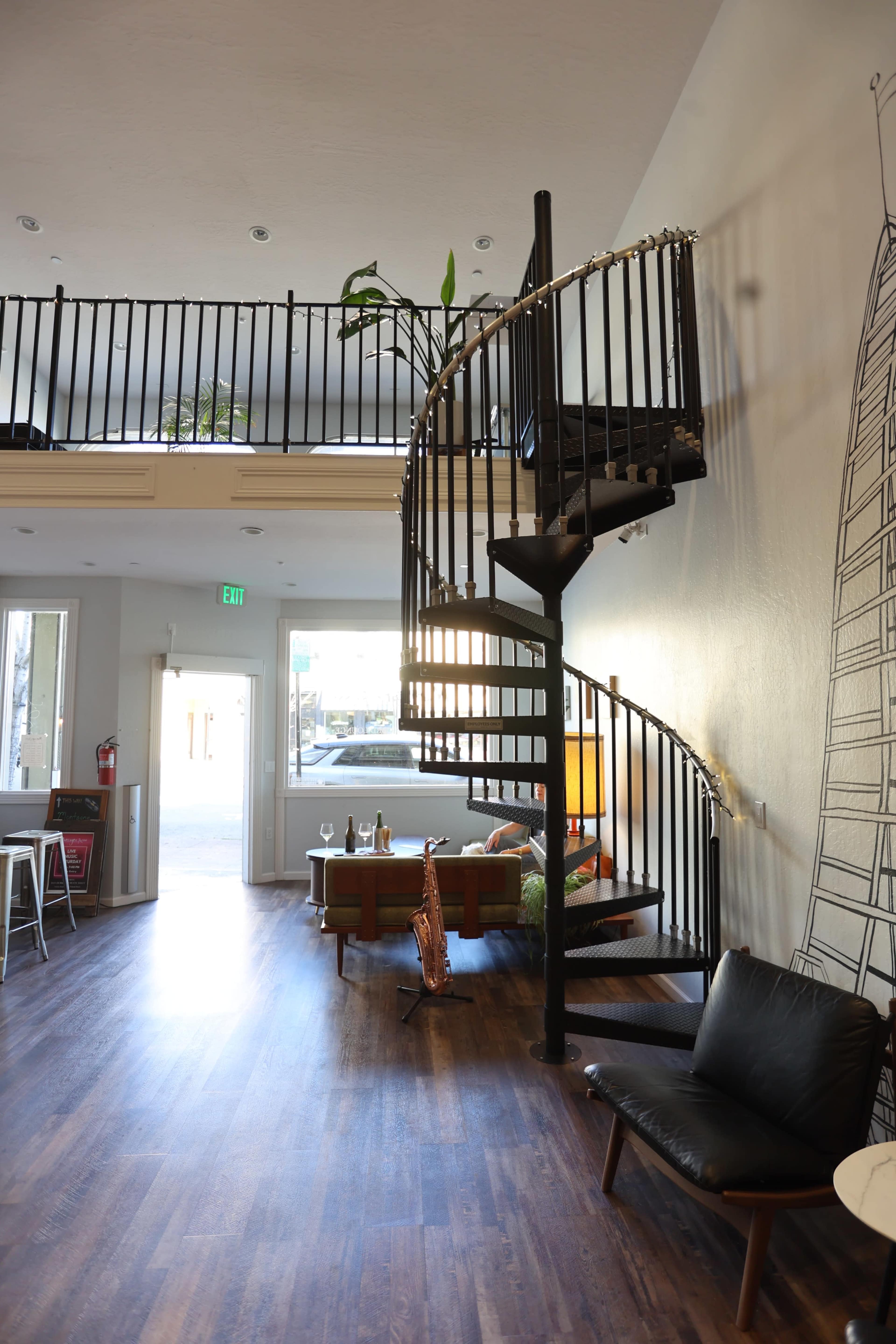 The image shows a modern interior with a spiral staircase leading to an upper level, surrounded by a seating area with a sofa and armchair.