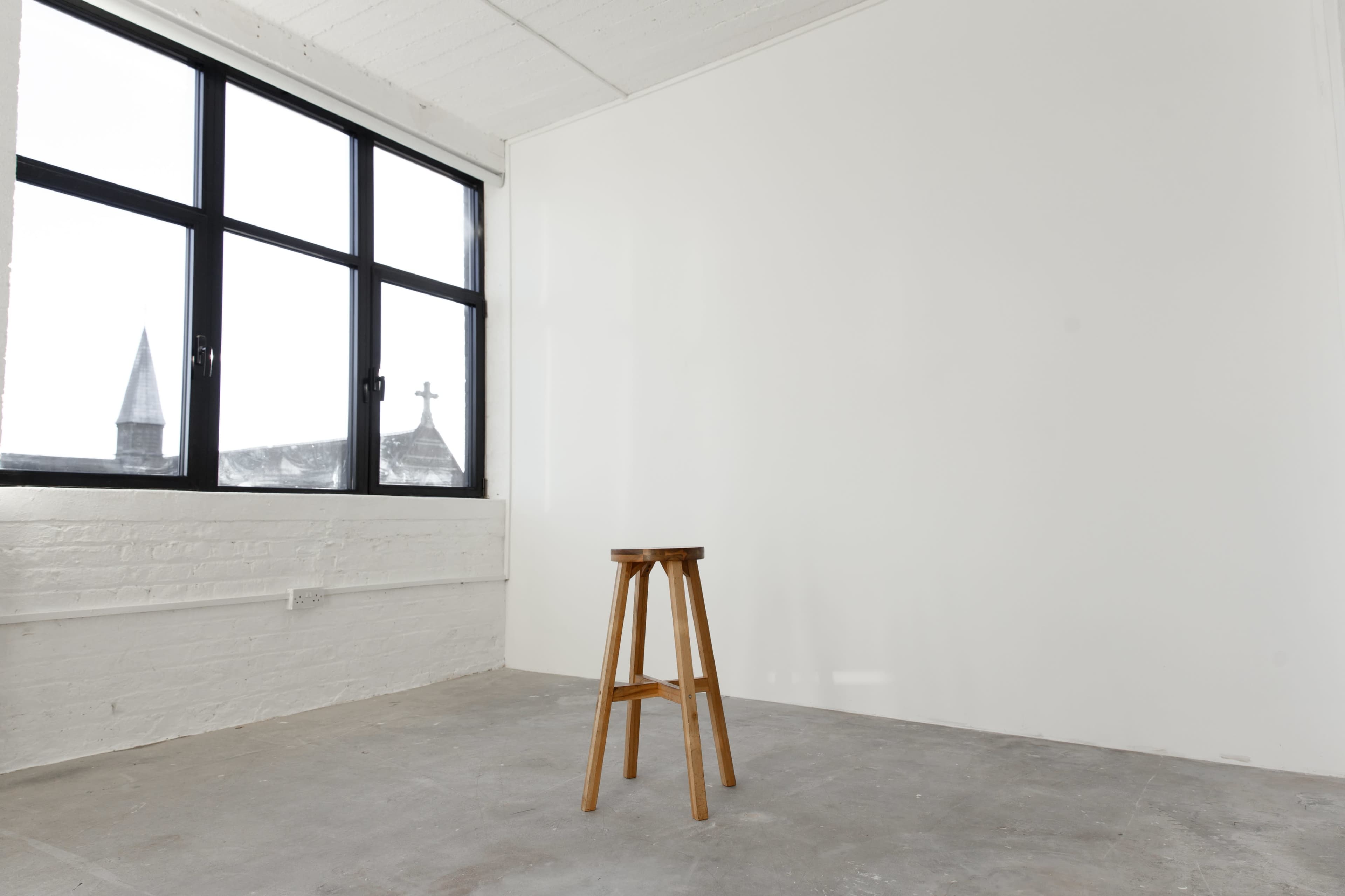 A bright, empty room with a wooden stool near a large window.