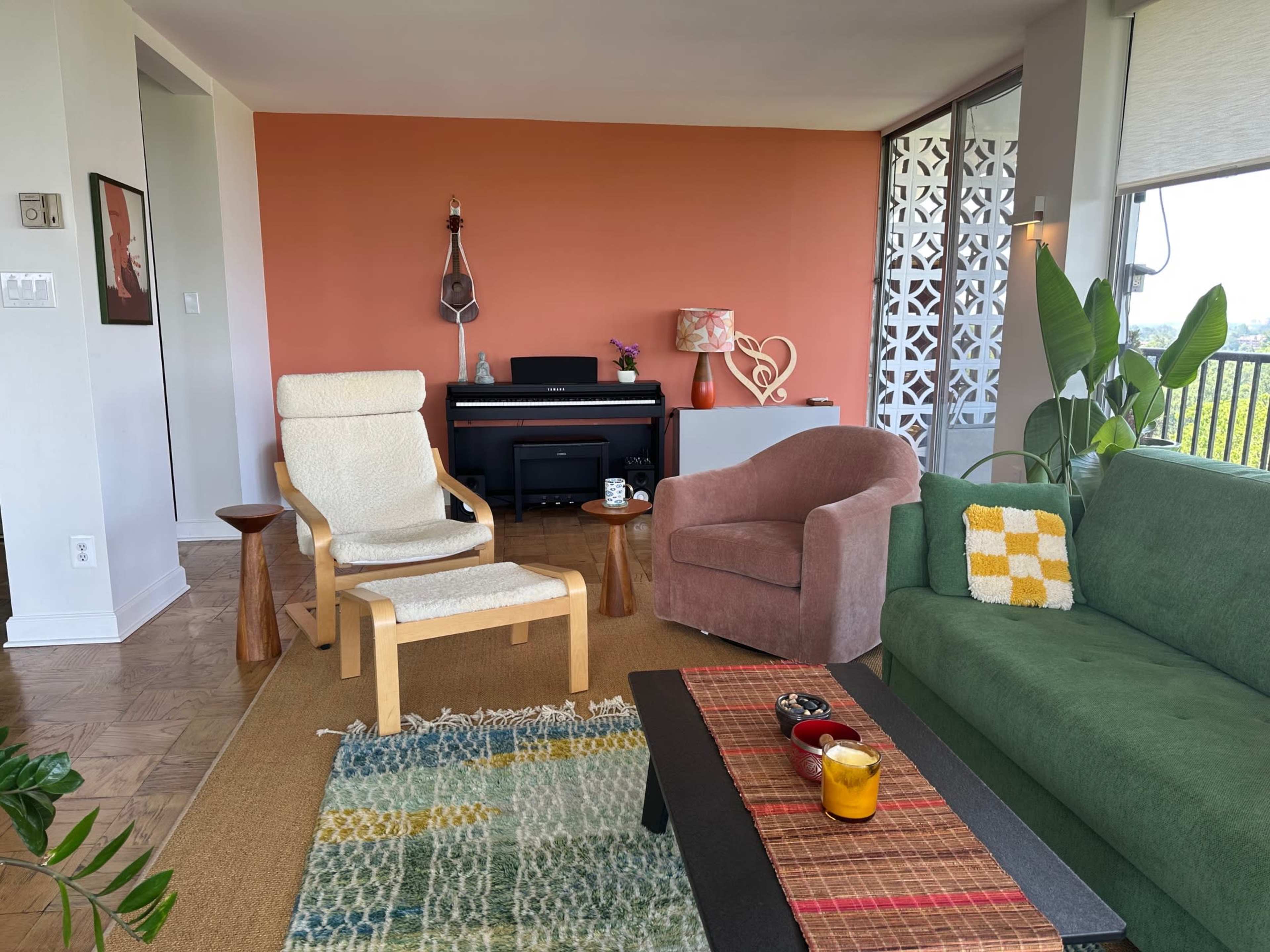 The living room features a green couch, a pink chair, a wooden side table, a beige recliner, and a small piano against a terracotta wall.
