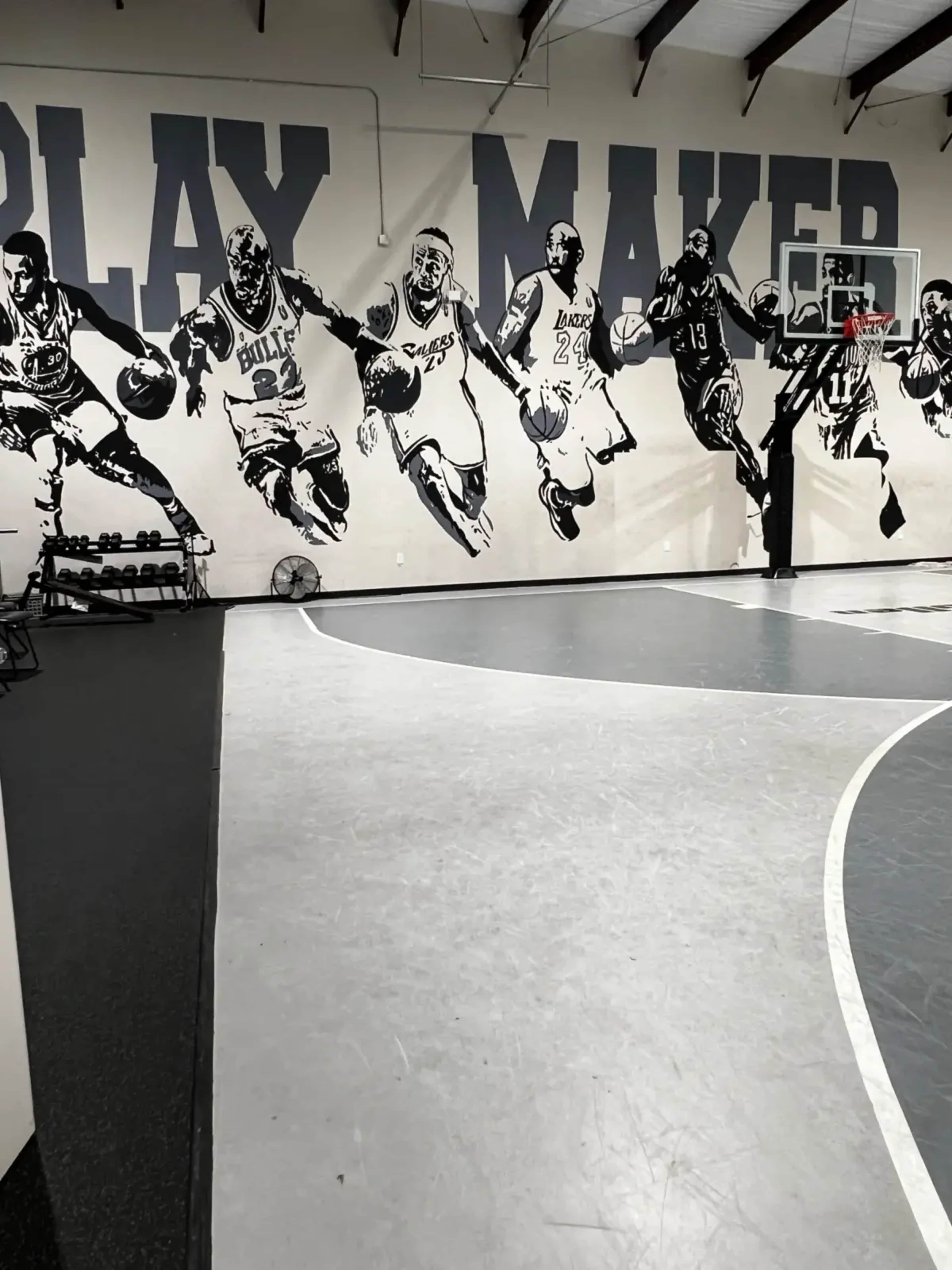 The image shows a basketball gym featuring a mural of players in action on the wall alongside a basketball hoop.