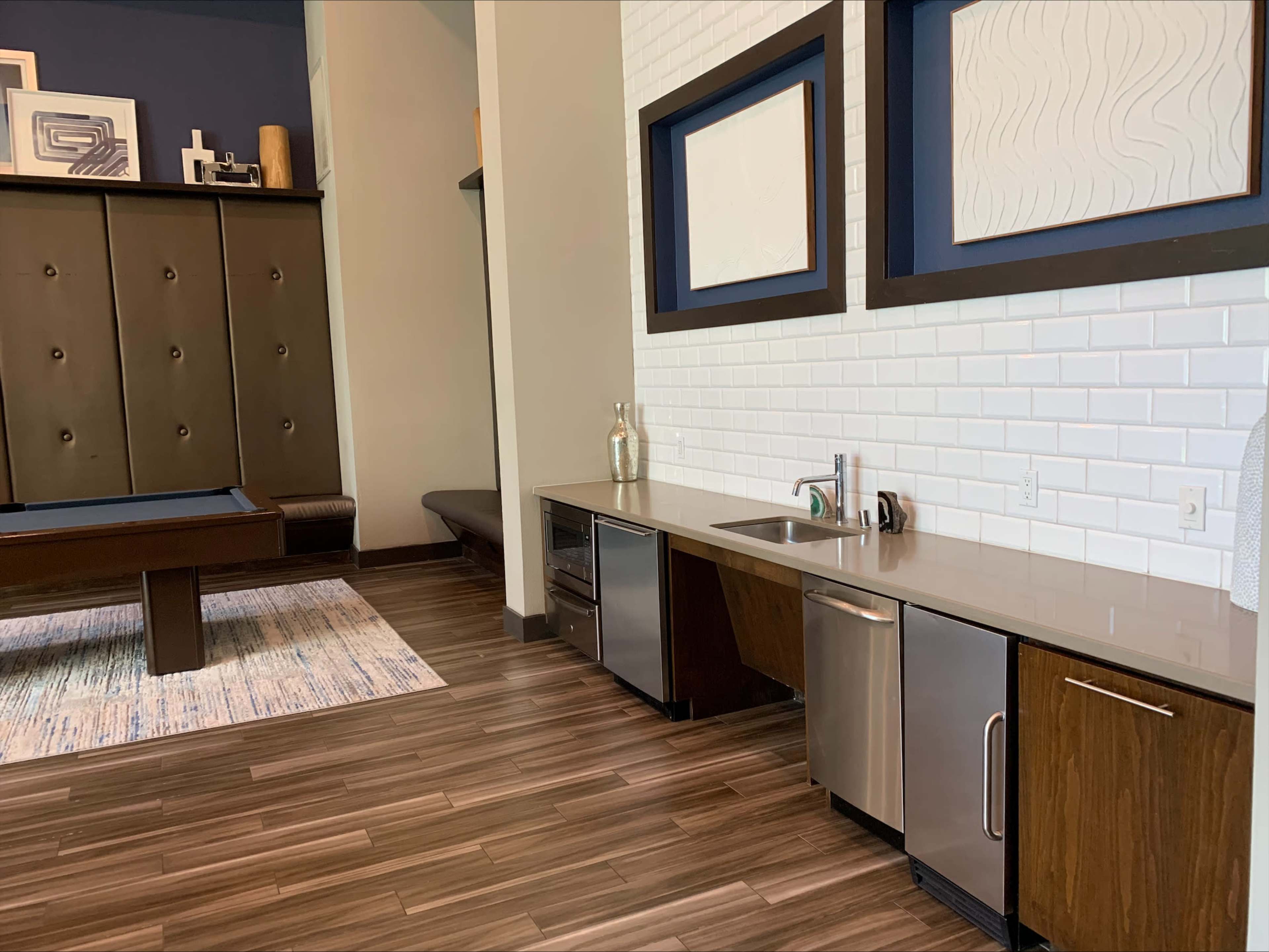 A modern kitchenette area with a sink and appliances next to a pool table in a stylish interior space.