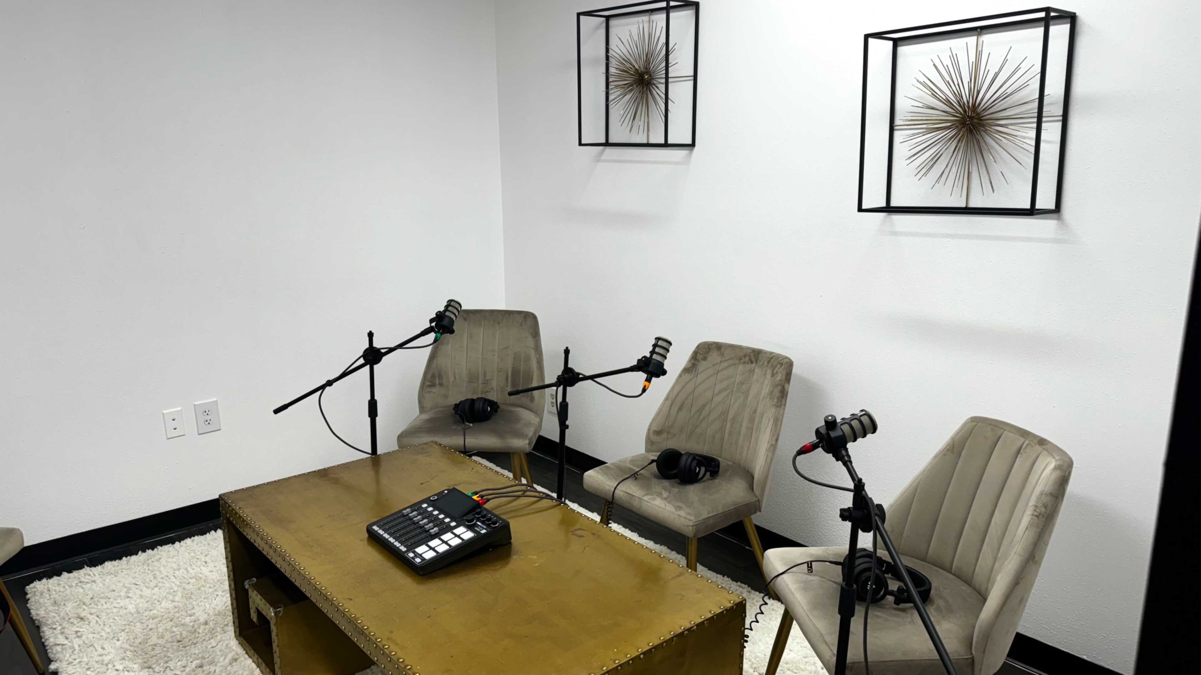A small recording studio features three chairs with microphones and headphones arranged around a table.