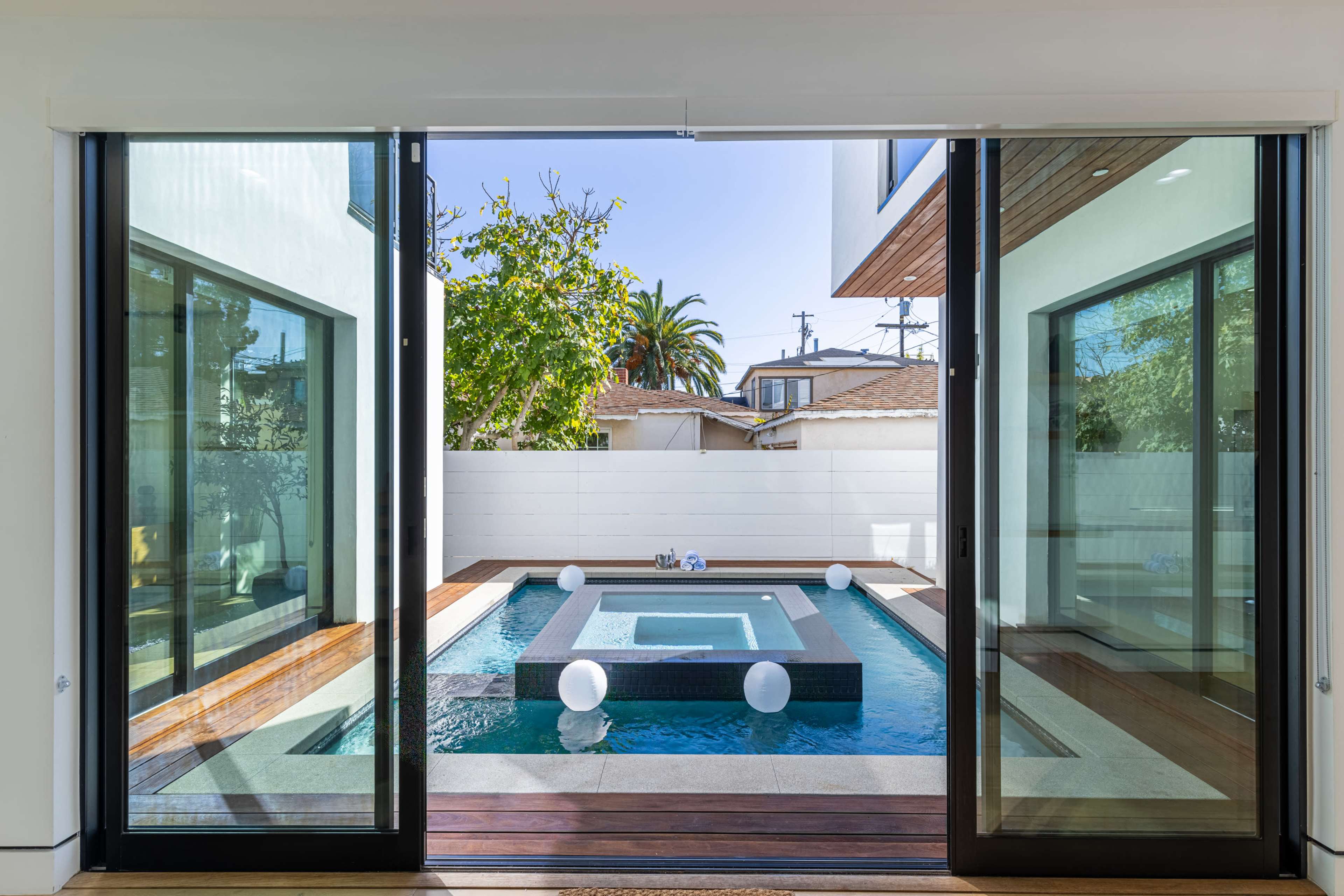 A modern home features large sliding glass doors that open to a serene backyard pool area with floating white spheres.