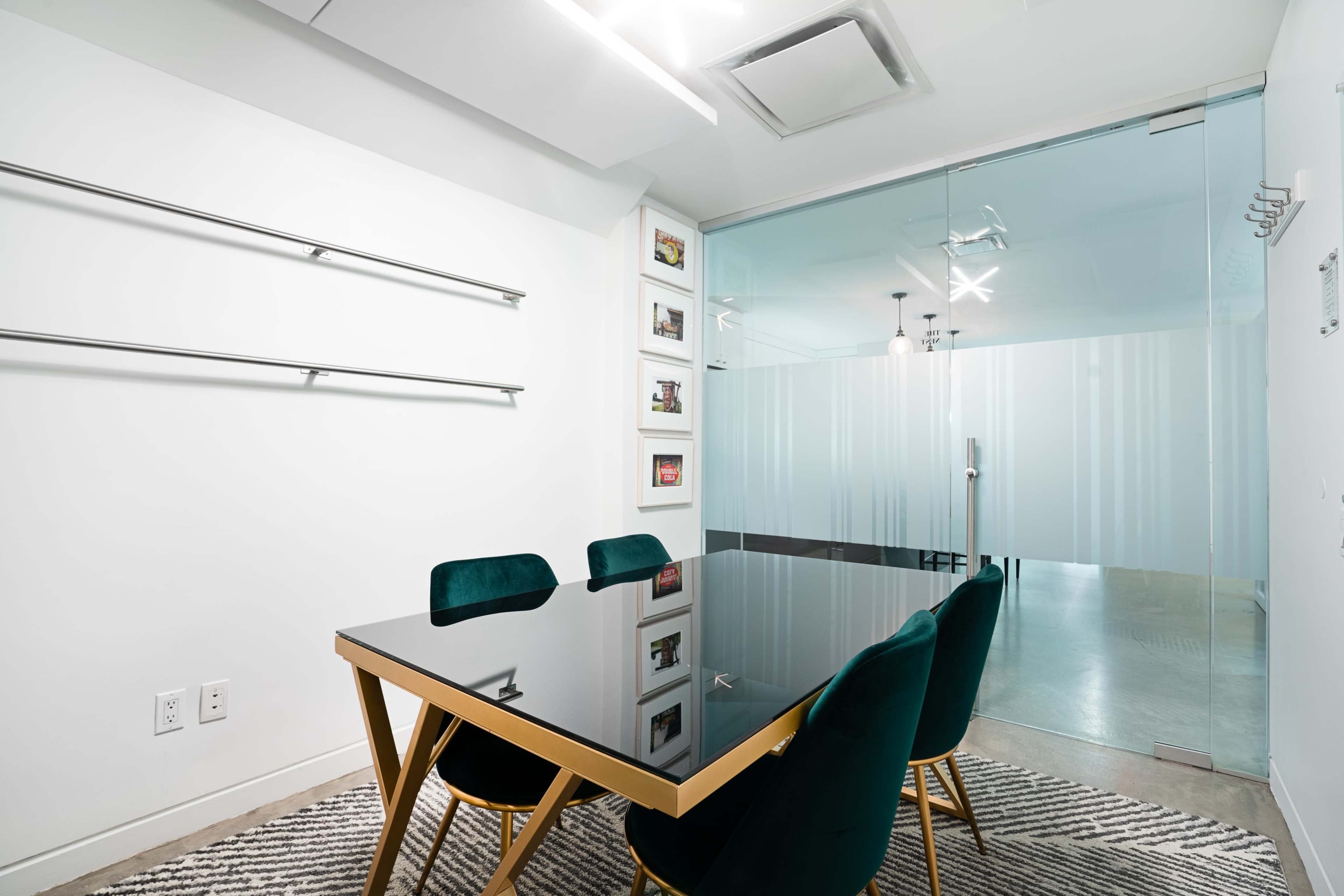 A modern meeting room features a rectangular black table surrounded by four green chairs, with glass walls and minimalist decor.