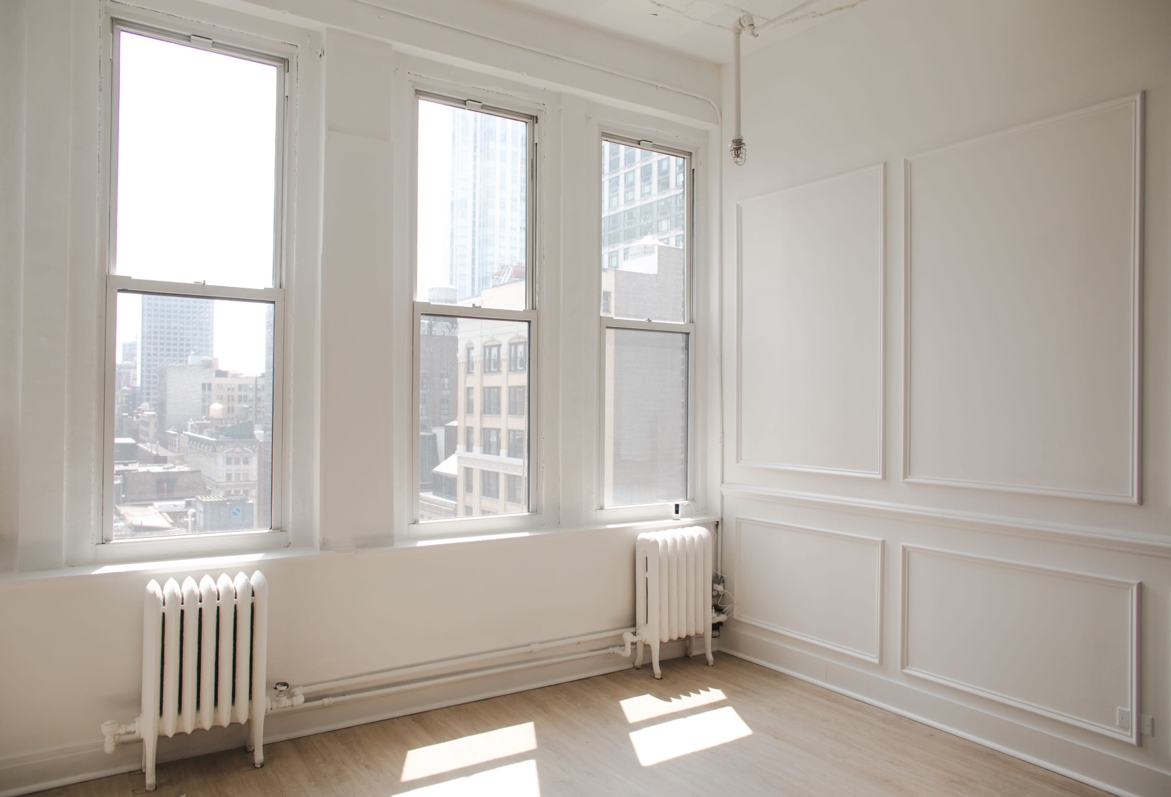 A bright, empty room features large windows and white walls with decorative trim.