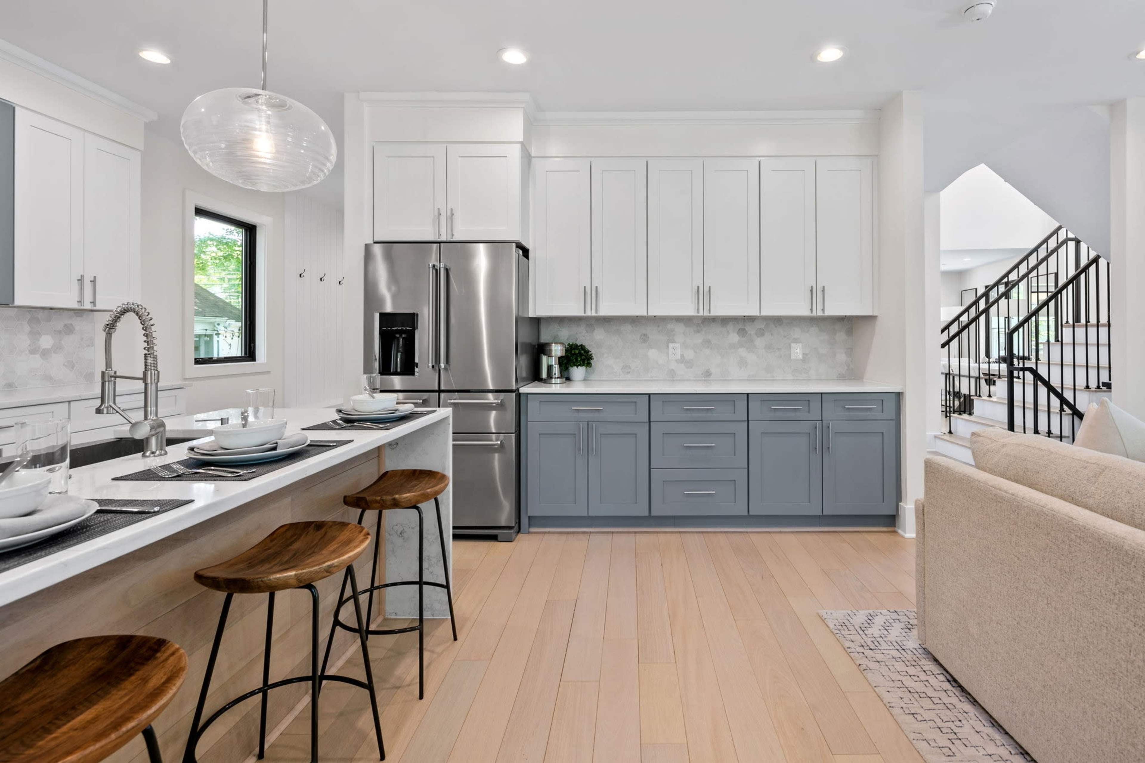 A modern kitchen featuring white cabinetry, stainless steel appliances, and a gray island with three wooden barstools.