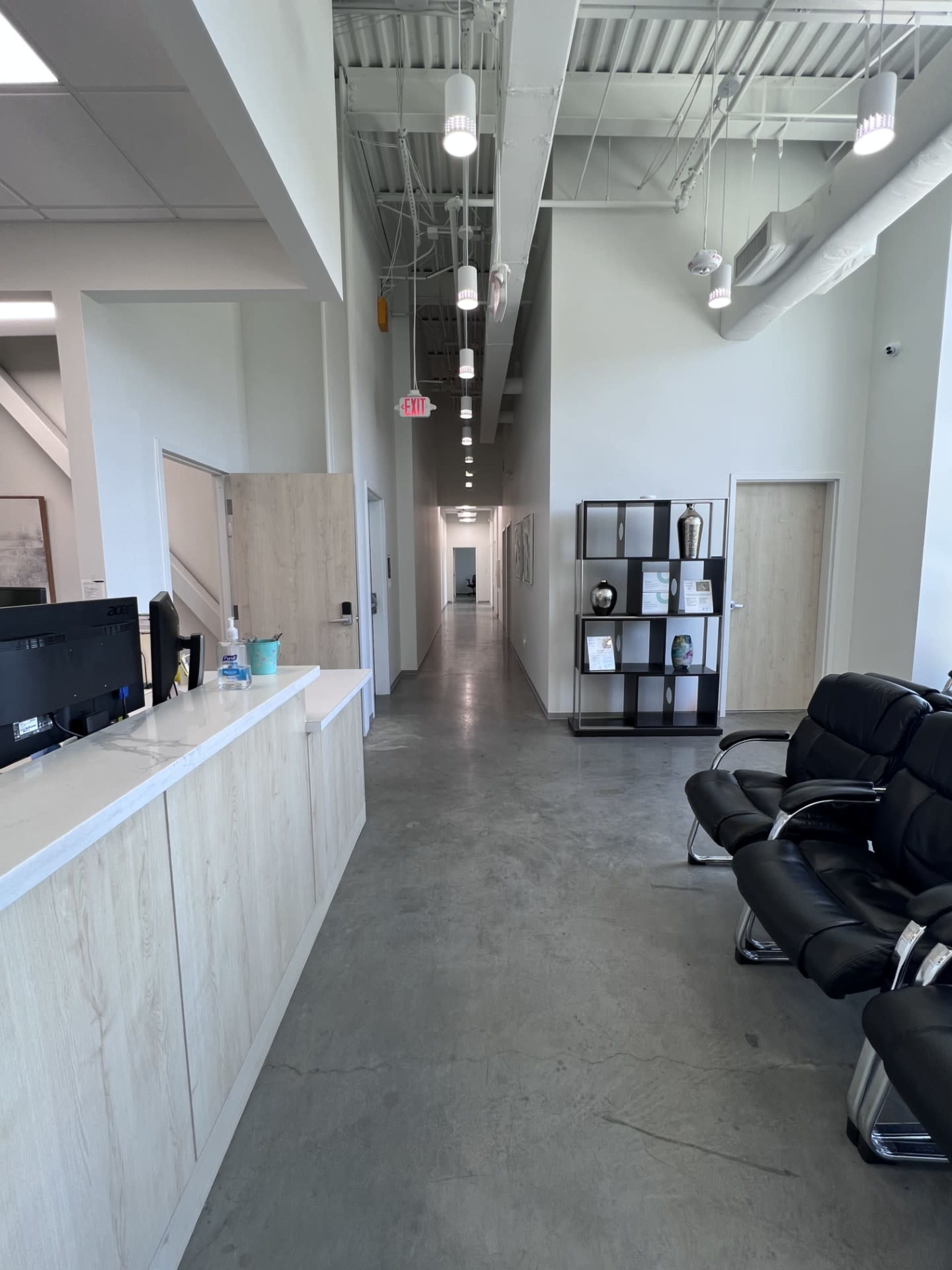 The image shows a modern reception area with a desk on the left and a long, well-lit corridor leading to other rooms at the end.