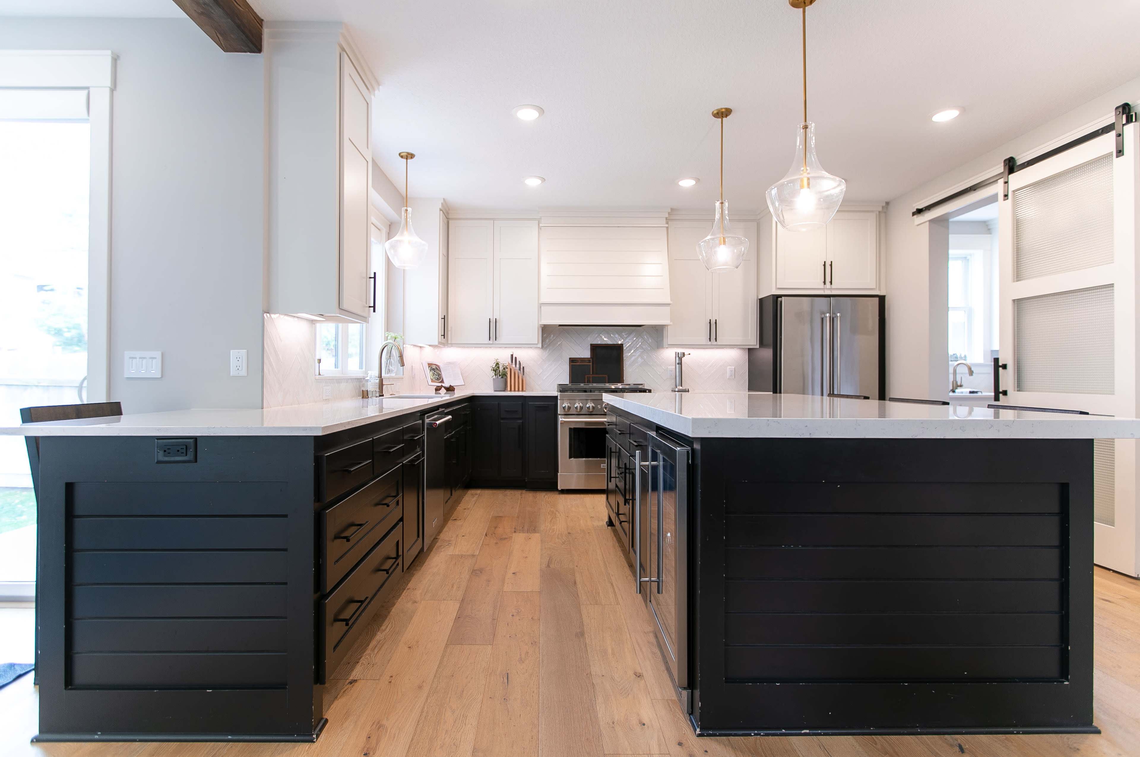 A modern kitchen featuring an island with black cabinetry, white countertops, and stainless steel appliances, with pendant lighting hanging above.