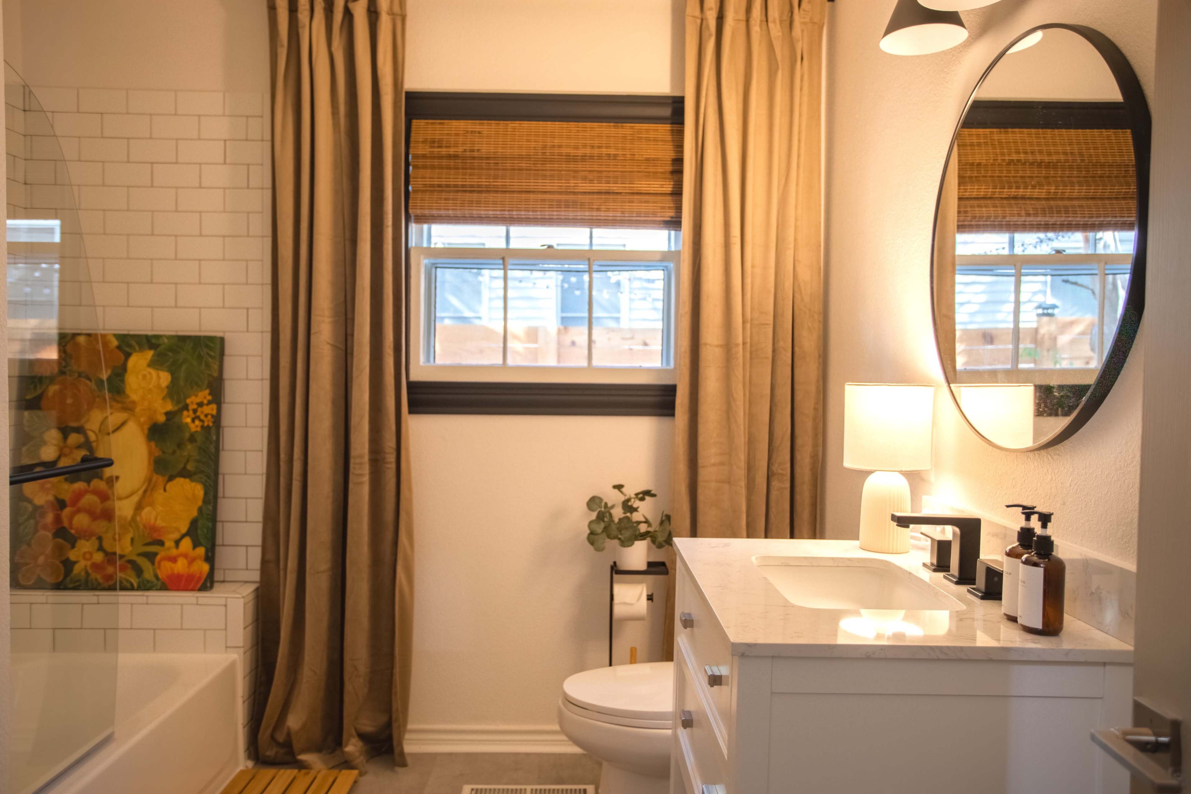 A bathroom featuring a bathtub, a sink with a large mirror, and beige curtains alongside a window.