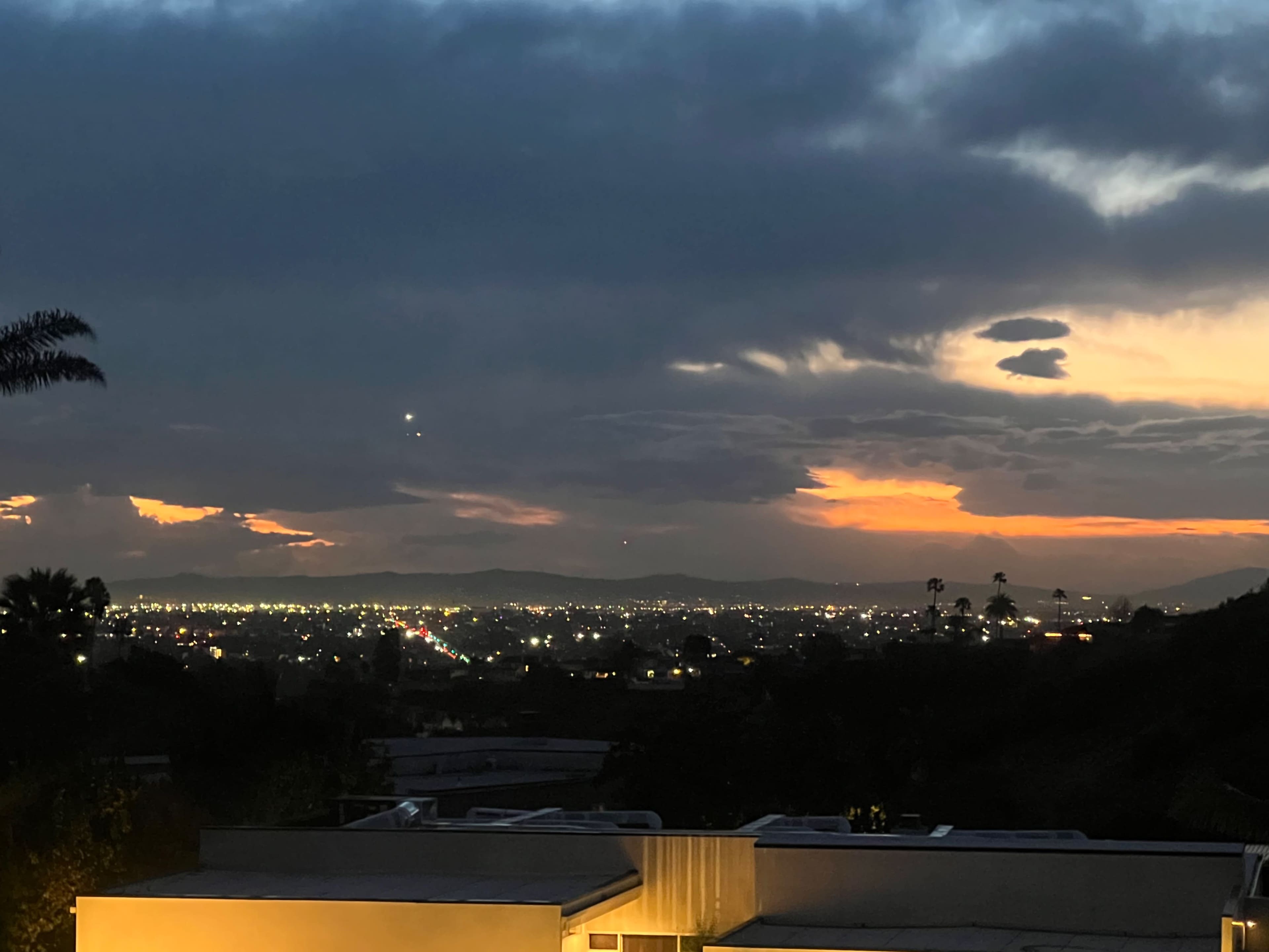 A cityscape at dusk with a view of lights and clouds against a colorful sunset sky.