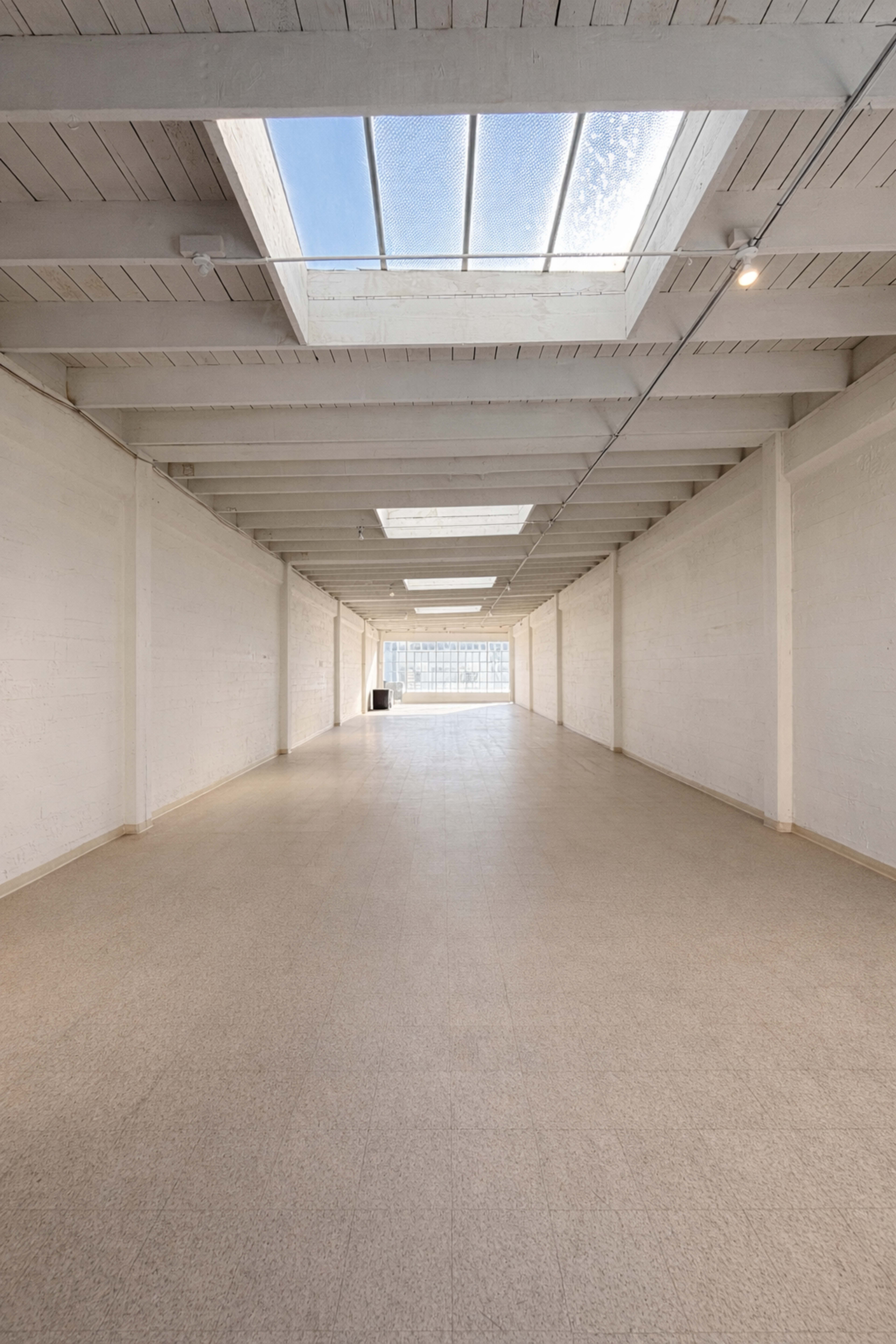 The image shows a long, empty corridor with large skylights along the ceiling.
