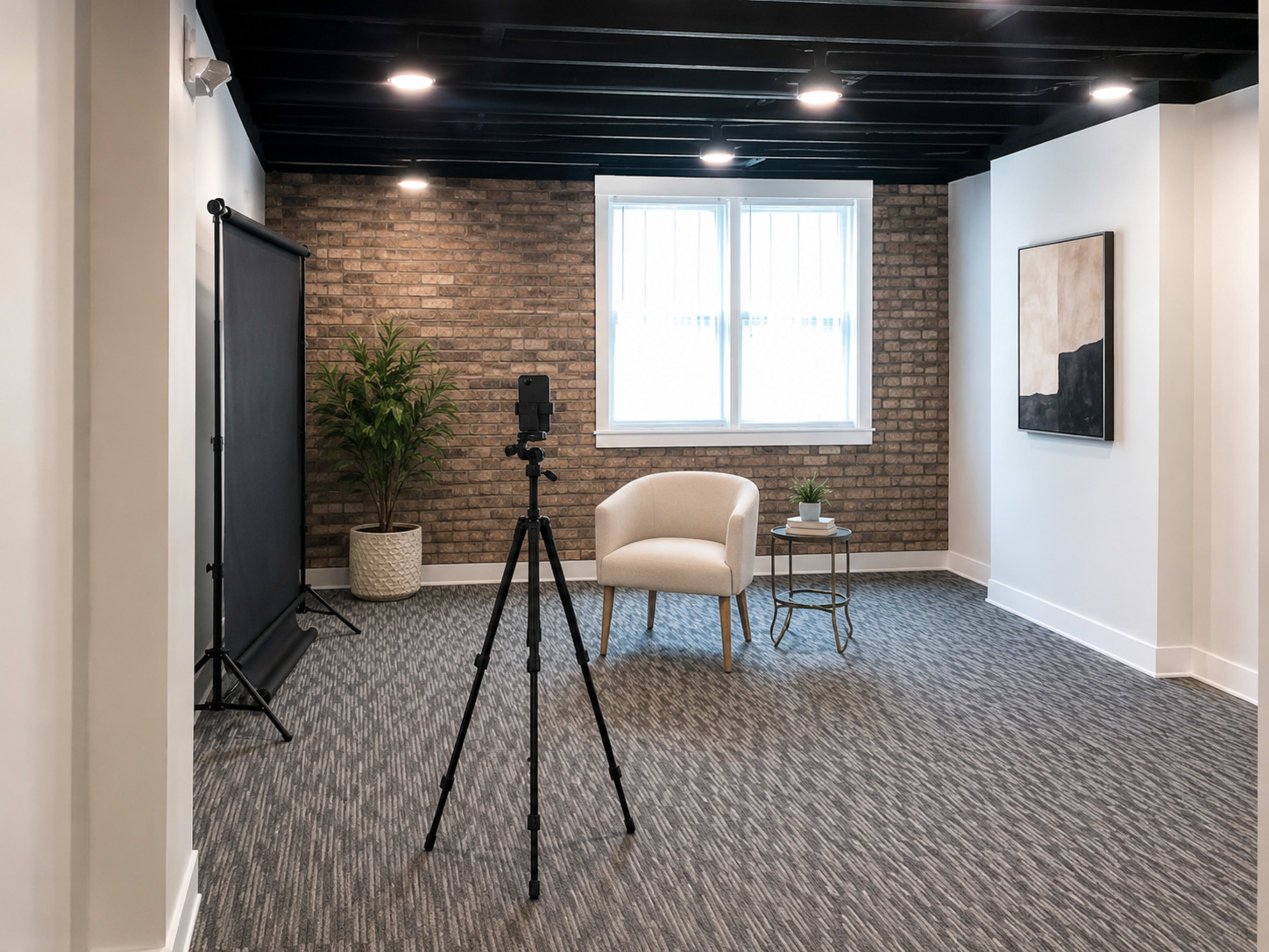 A minimalist styled room features a tripod with a camera facing a light-colored chair and a small table, situated against a textured brick wall.