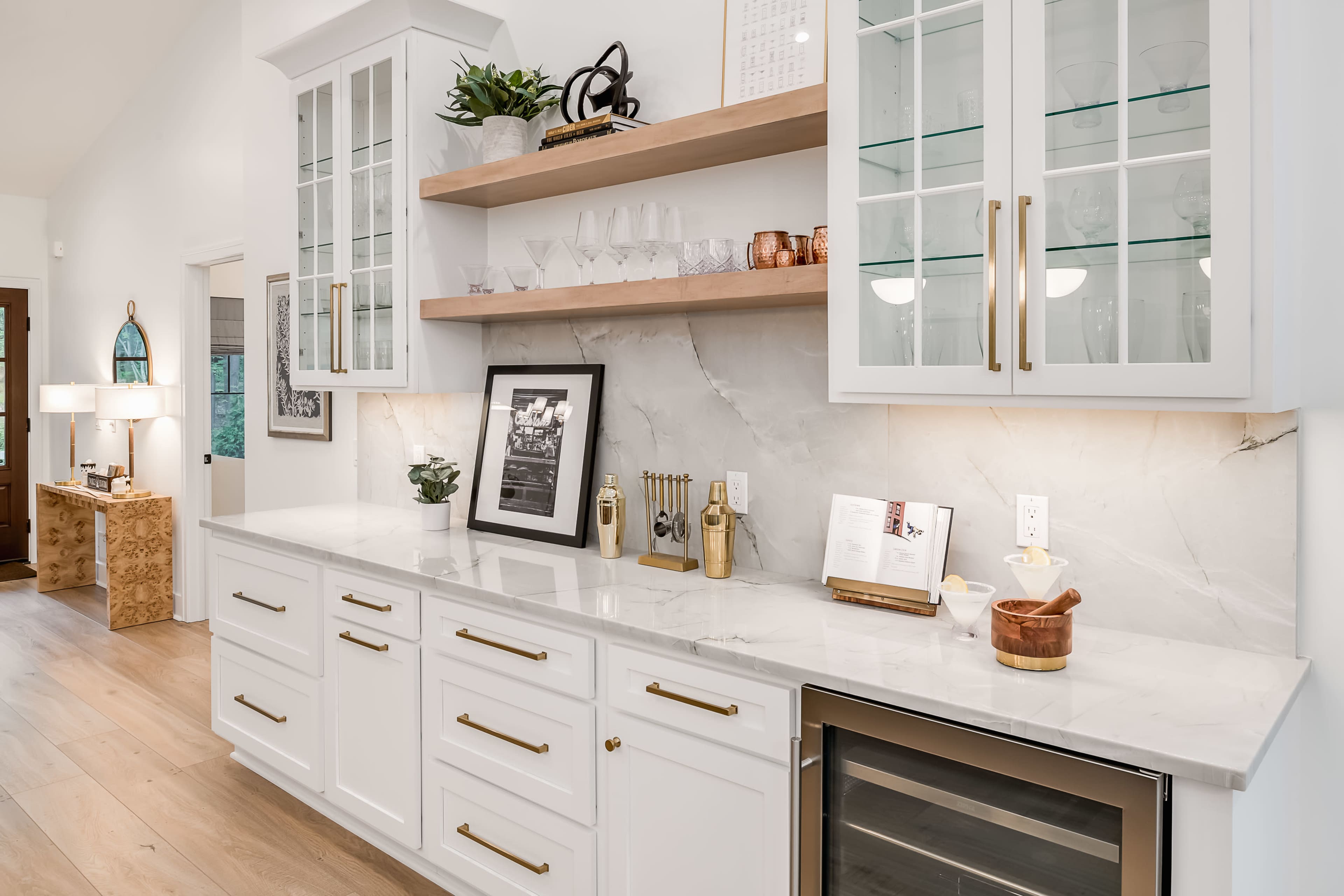 A modern kitchen space with white cabinetry, a marble countertop, and an under-counter wine fridge.