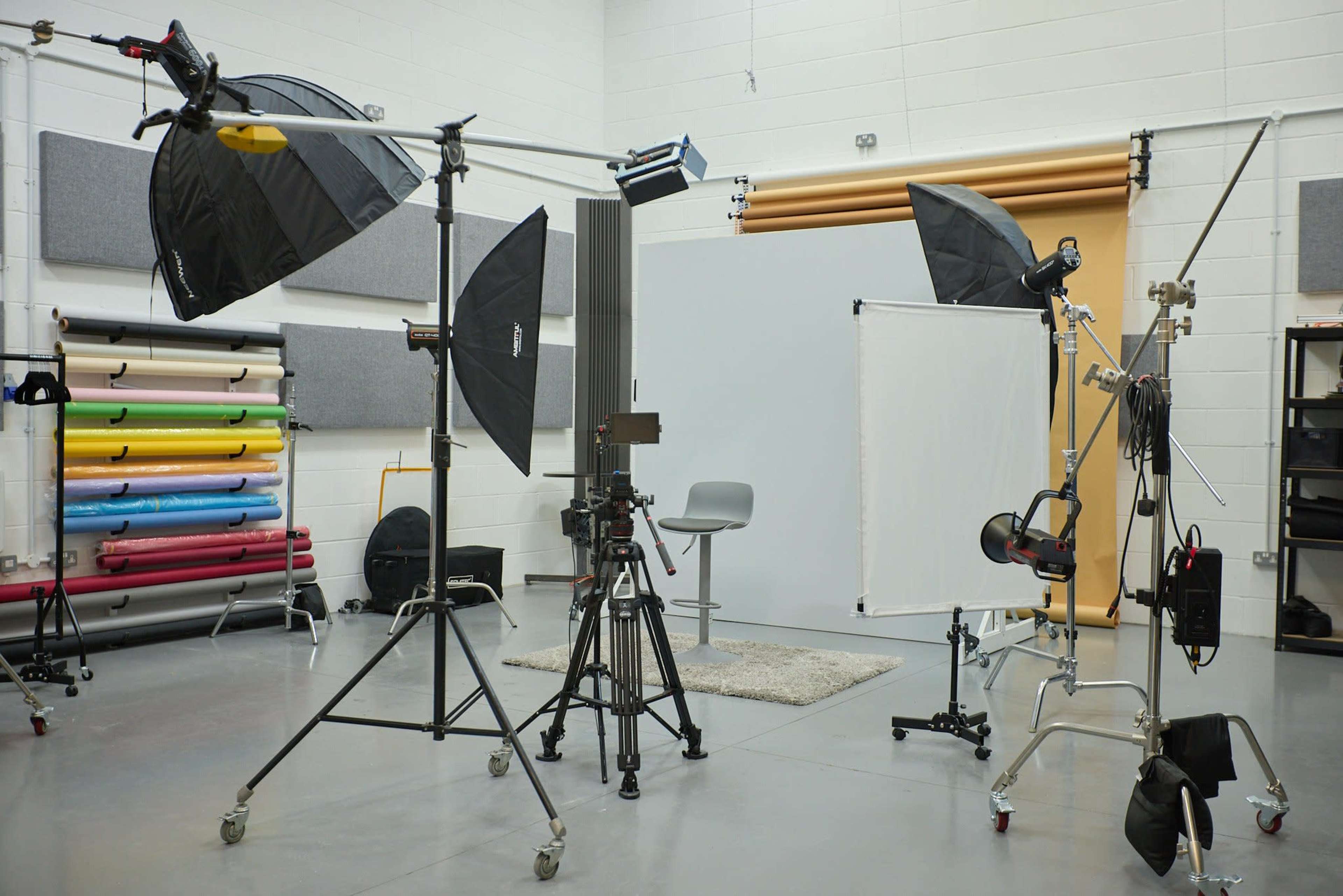 A photography studio is set up with various lighting equipment, backdrops, and a chair on a gray floor.