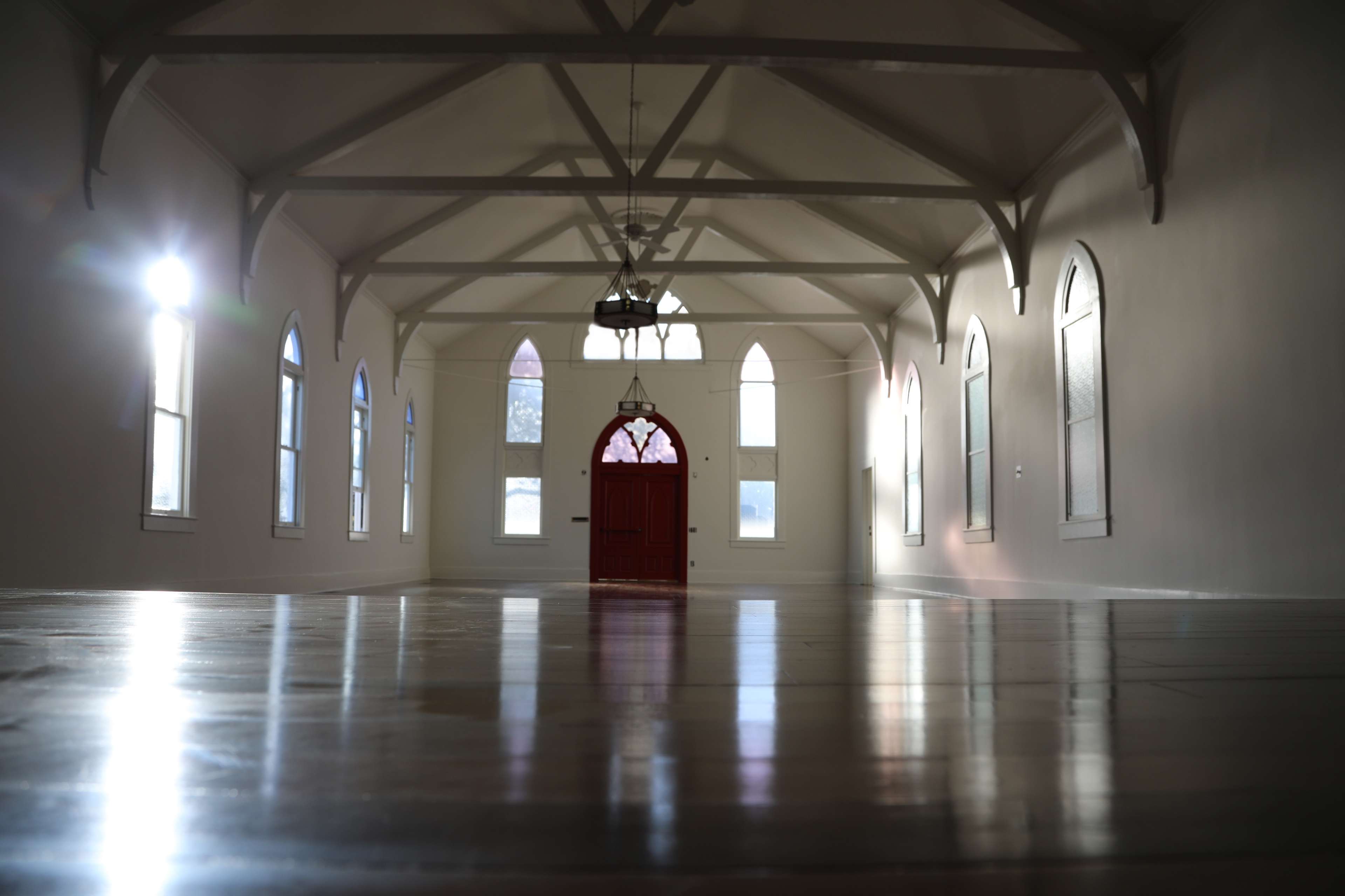 A spacious, brightly lit room with arched windows and a red door at one end.