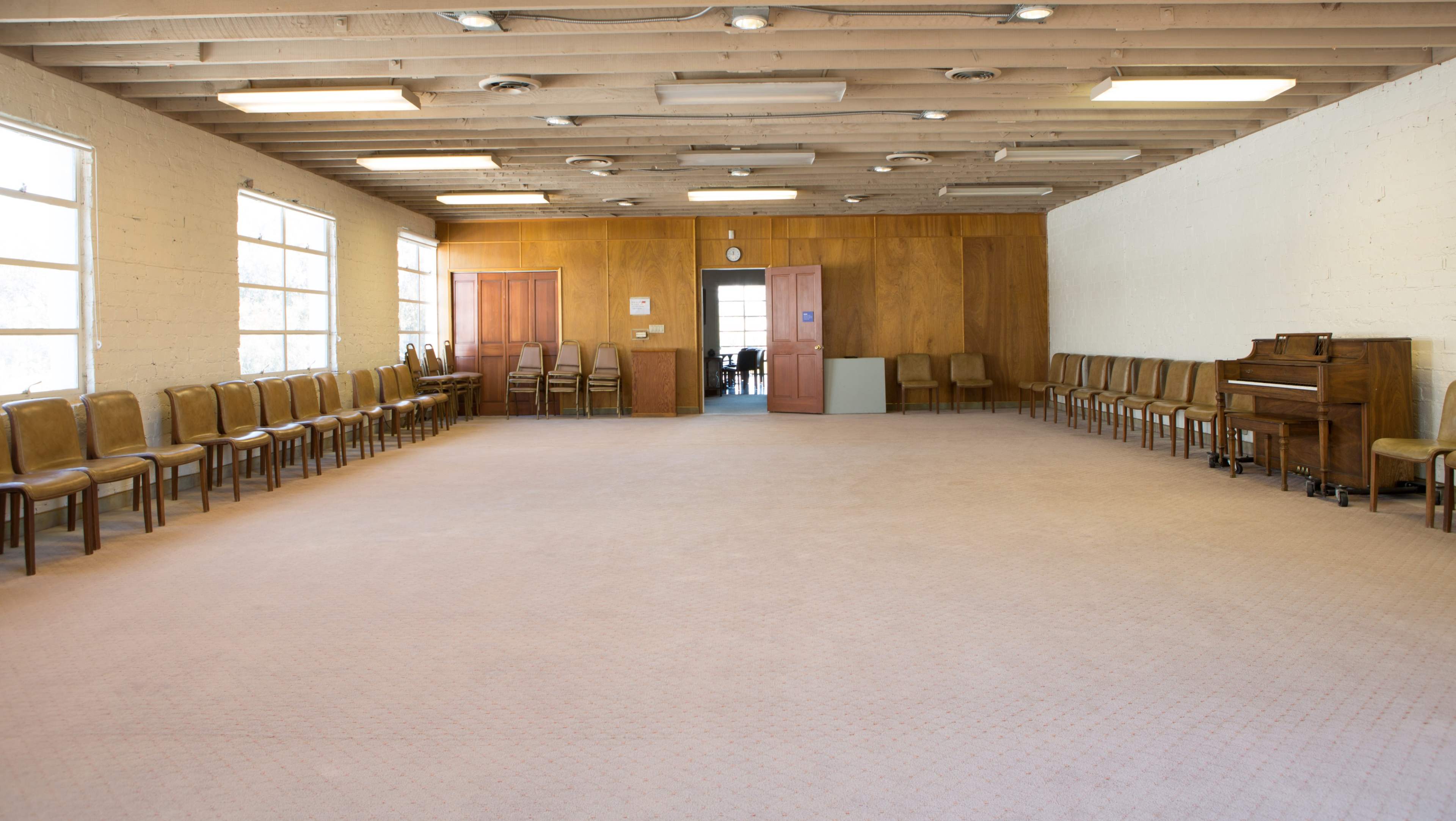 A sparsely furnished room with rows of chairs lining the walls and a piano positioned in one corner.