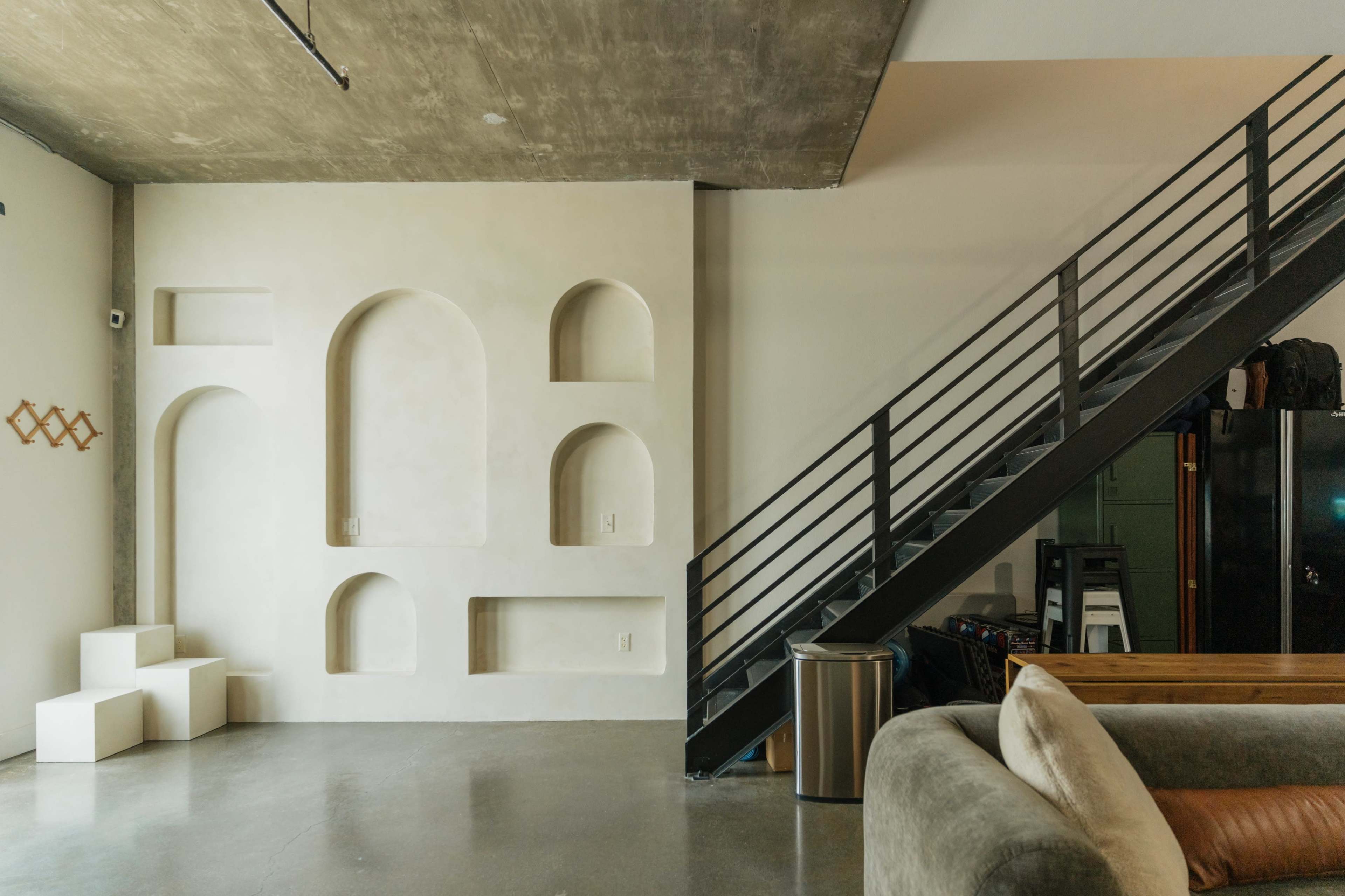 The image features an interior space with a textured wall showcasing curved recesses and a metal staircase leading to an upper level.