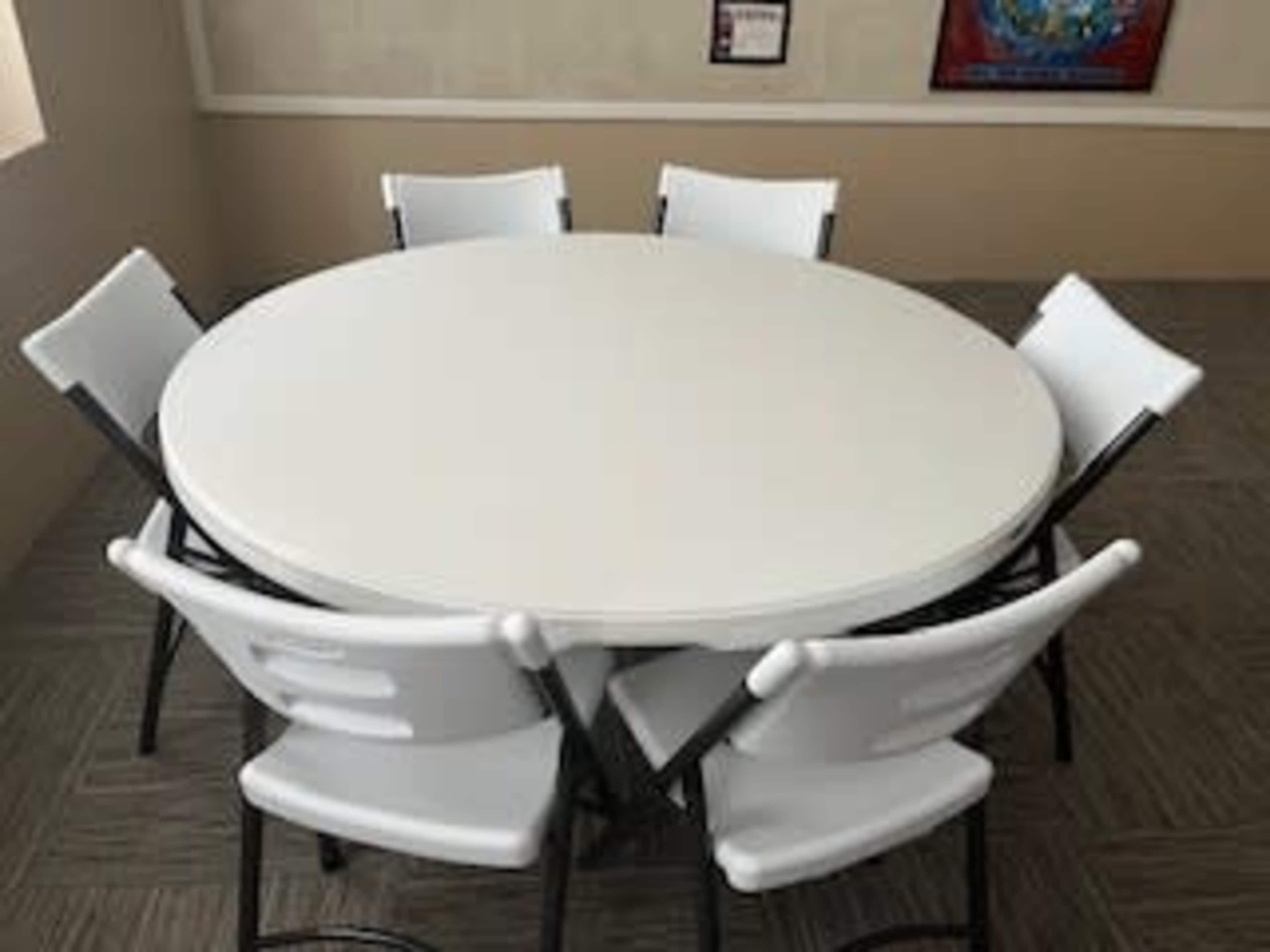 A round white table is surrounded by six folding chairs in a well-lit indoor setting.