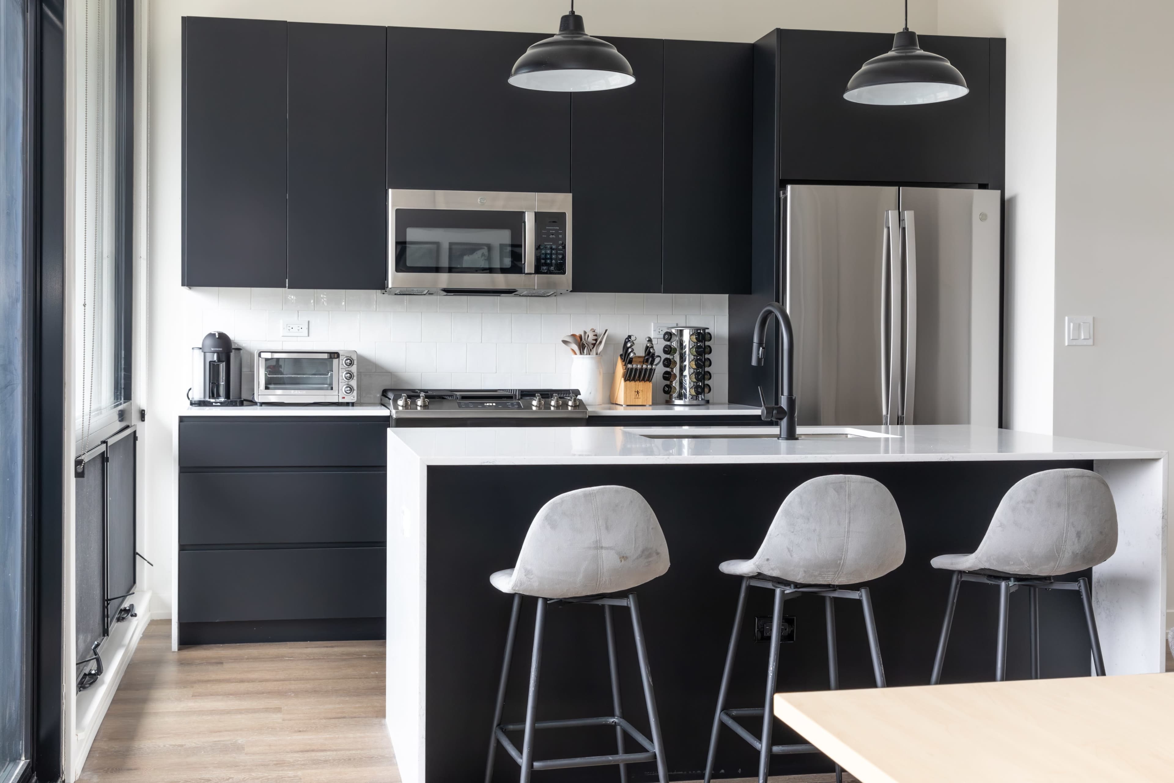 A modern kitchen features black cabinetry, stainless steel appliances, and a white island with bar stools.