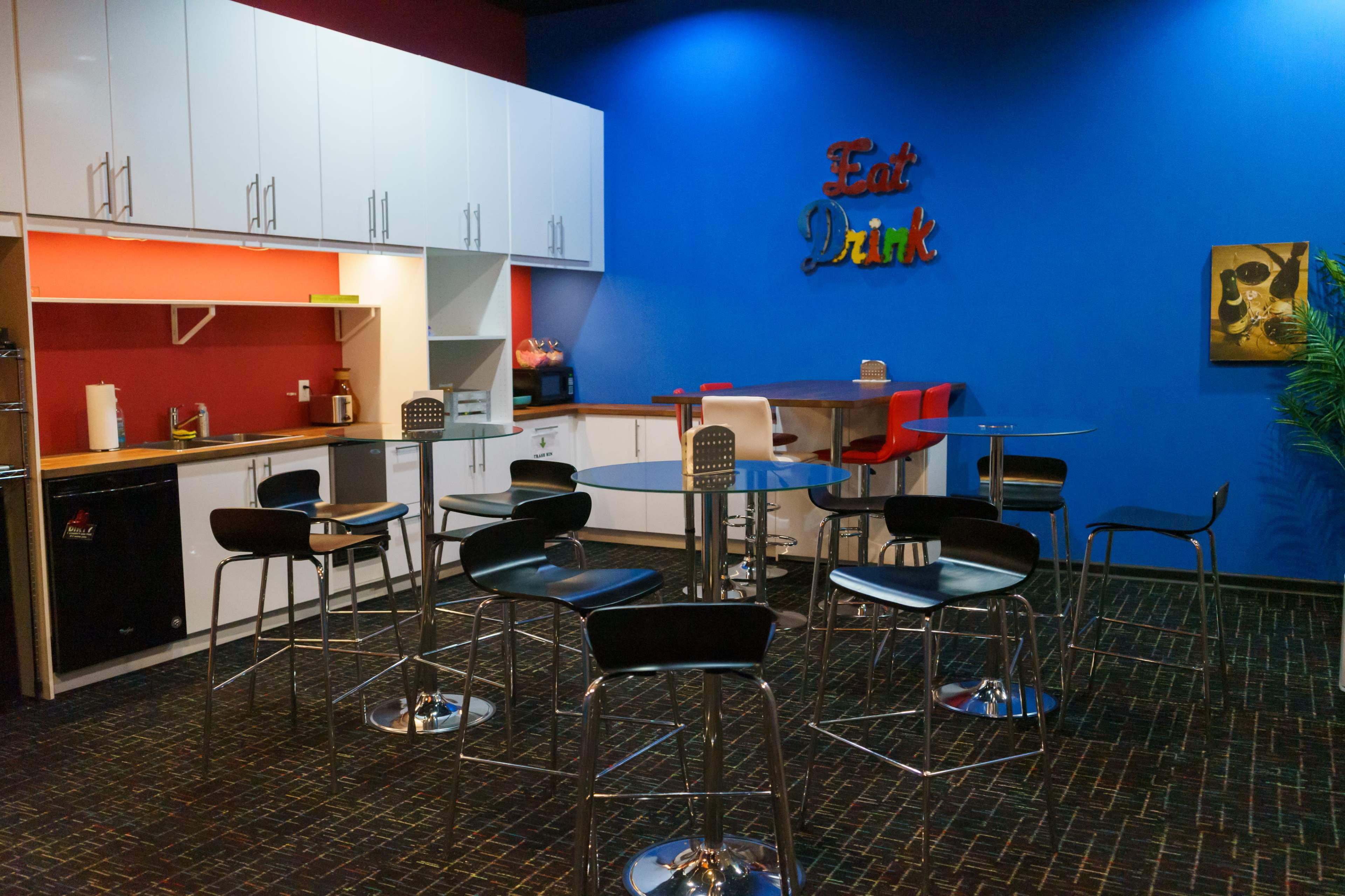 A sleek break room features a collection of black bar stools around circular tables, with modern cabinetry and colorful walls.