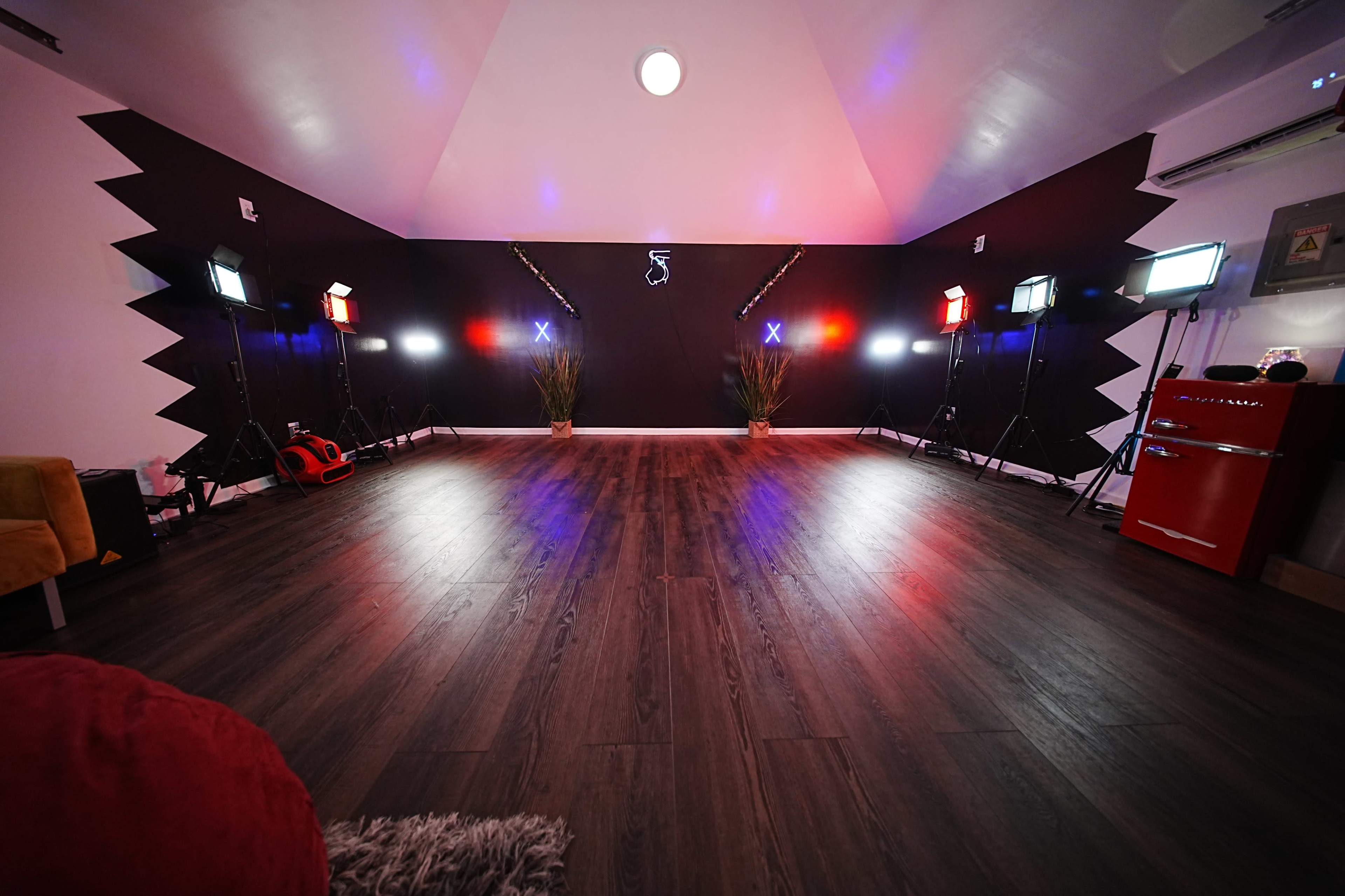 The image shows a spacious studio room with a dark wall accentuated by colorful lighting and several floor-mounted studio lights.