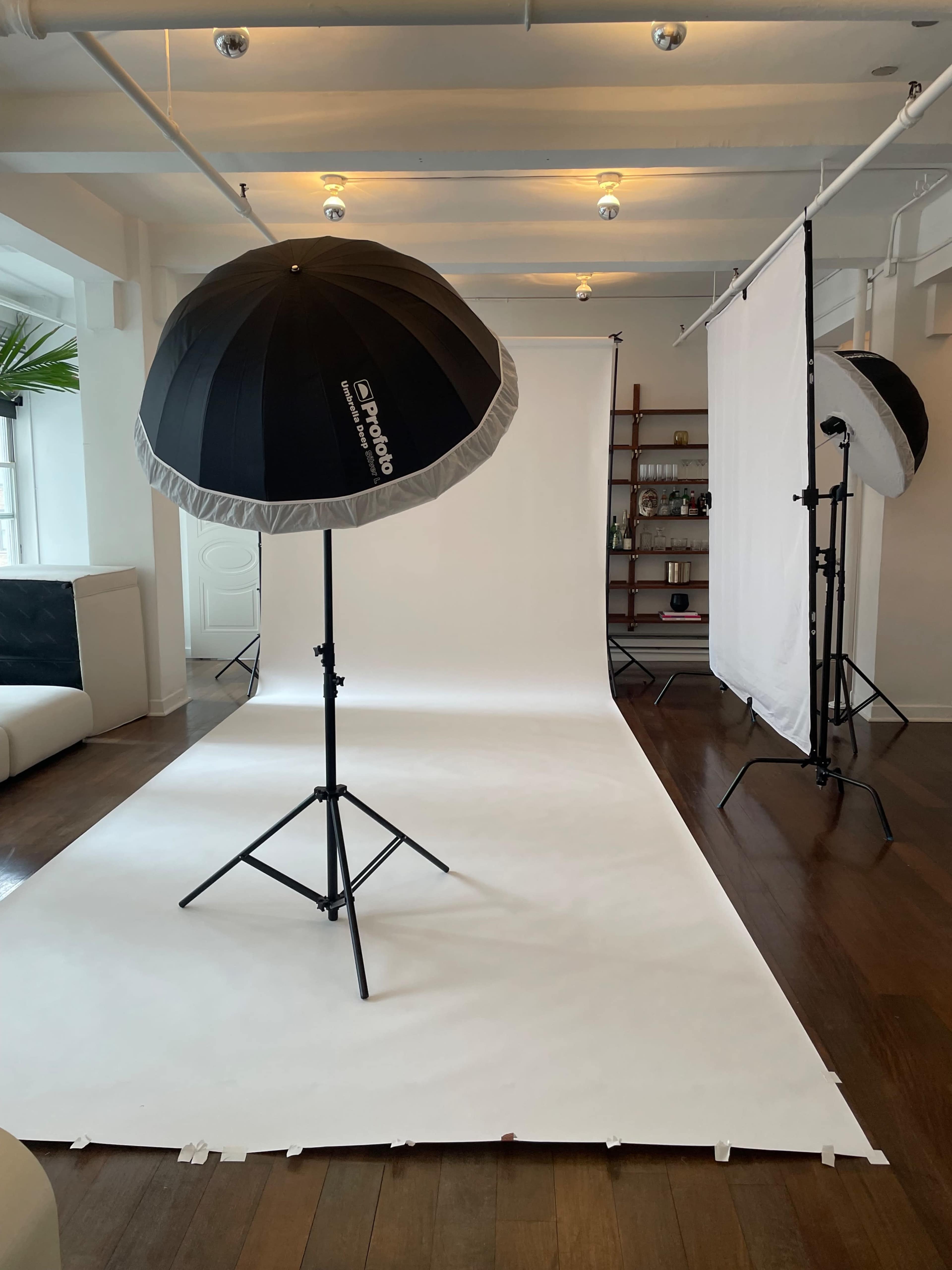 A photography studio with white backdrops and soft umbrella lights set up on stands.
