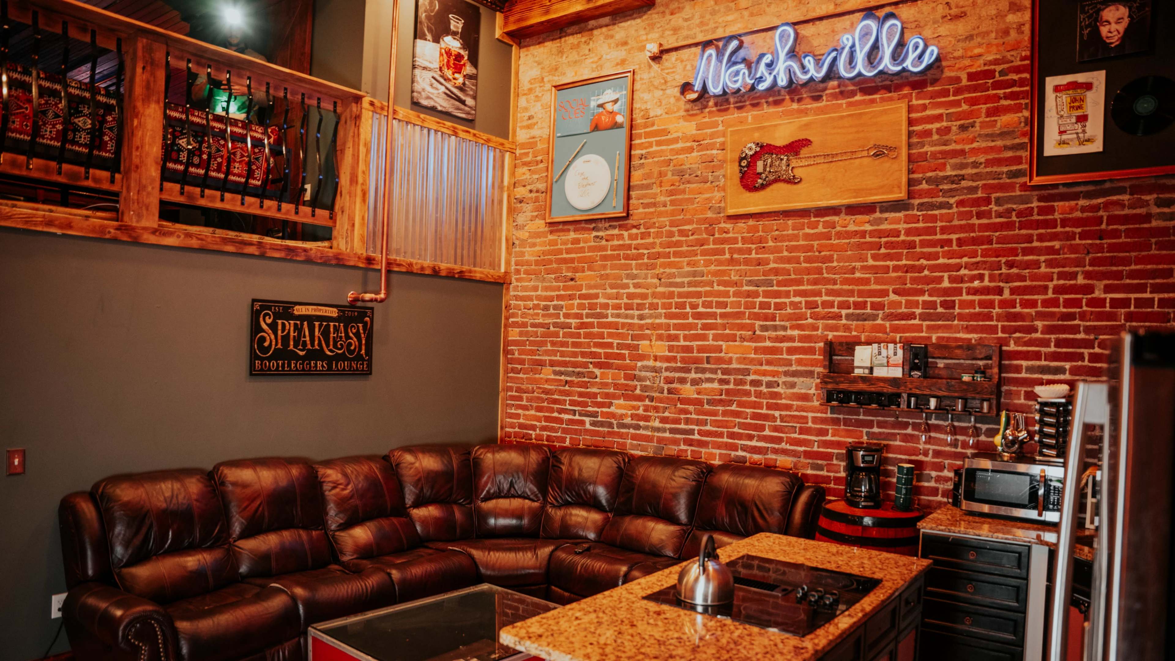 The interior features a cozy seating area with a dark leather couch, a granite coffee table, and a wall adorned with exposed brick and various musical decorations, including a neon sign that says "Nashville."