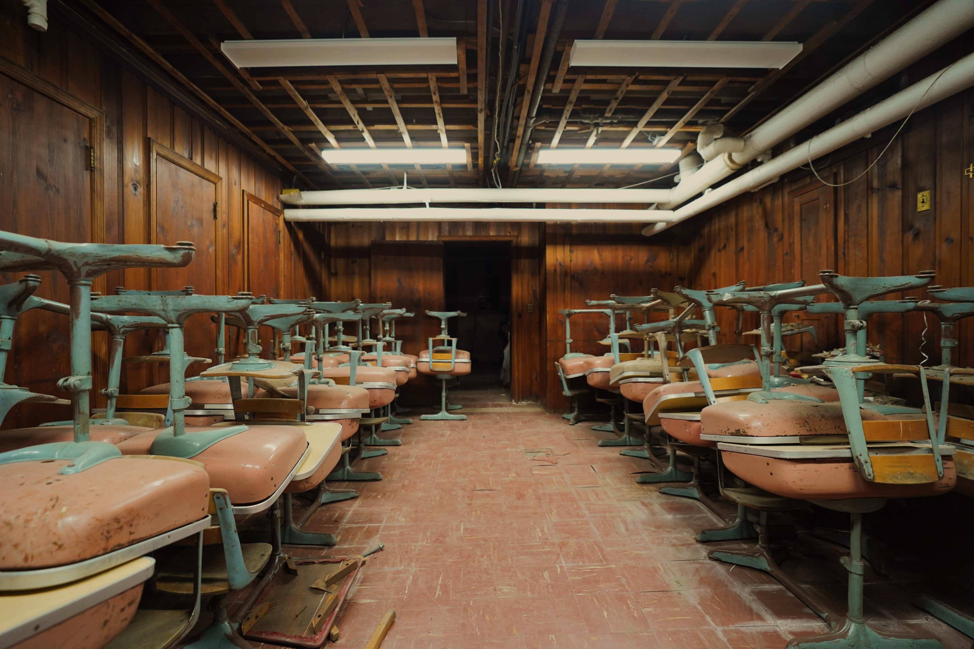 An abandoned classroom with overturned pink chairs arranged in rows against wooden walls.
