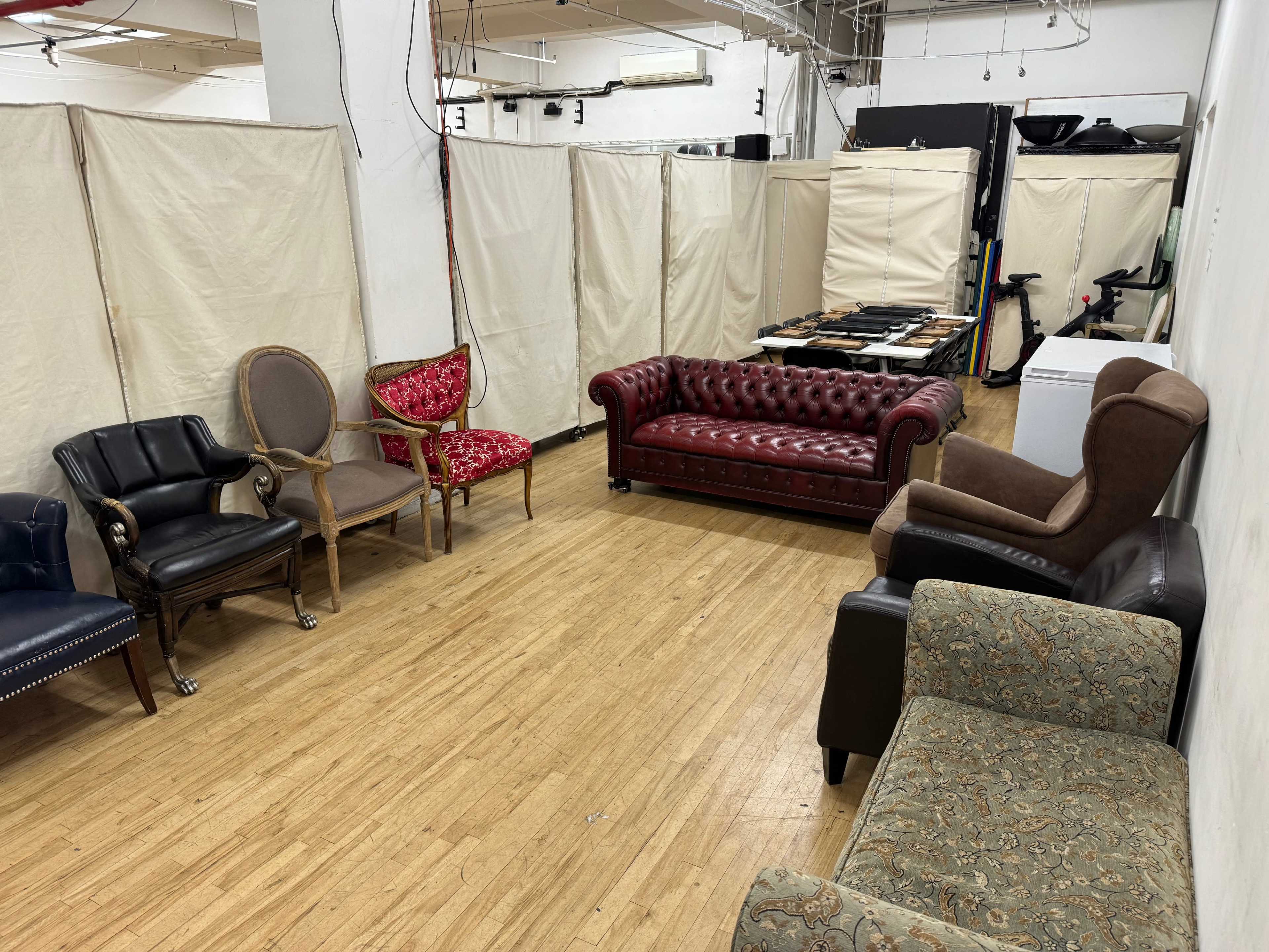 The image shows a collection of various upholstered chairs and sofas arranged in a large room with partitioned areas.