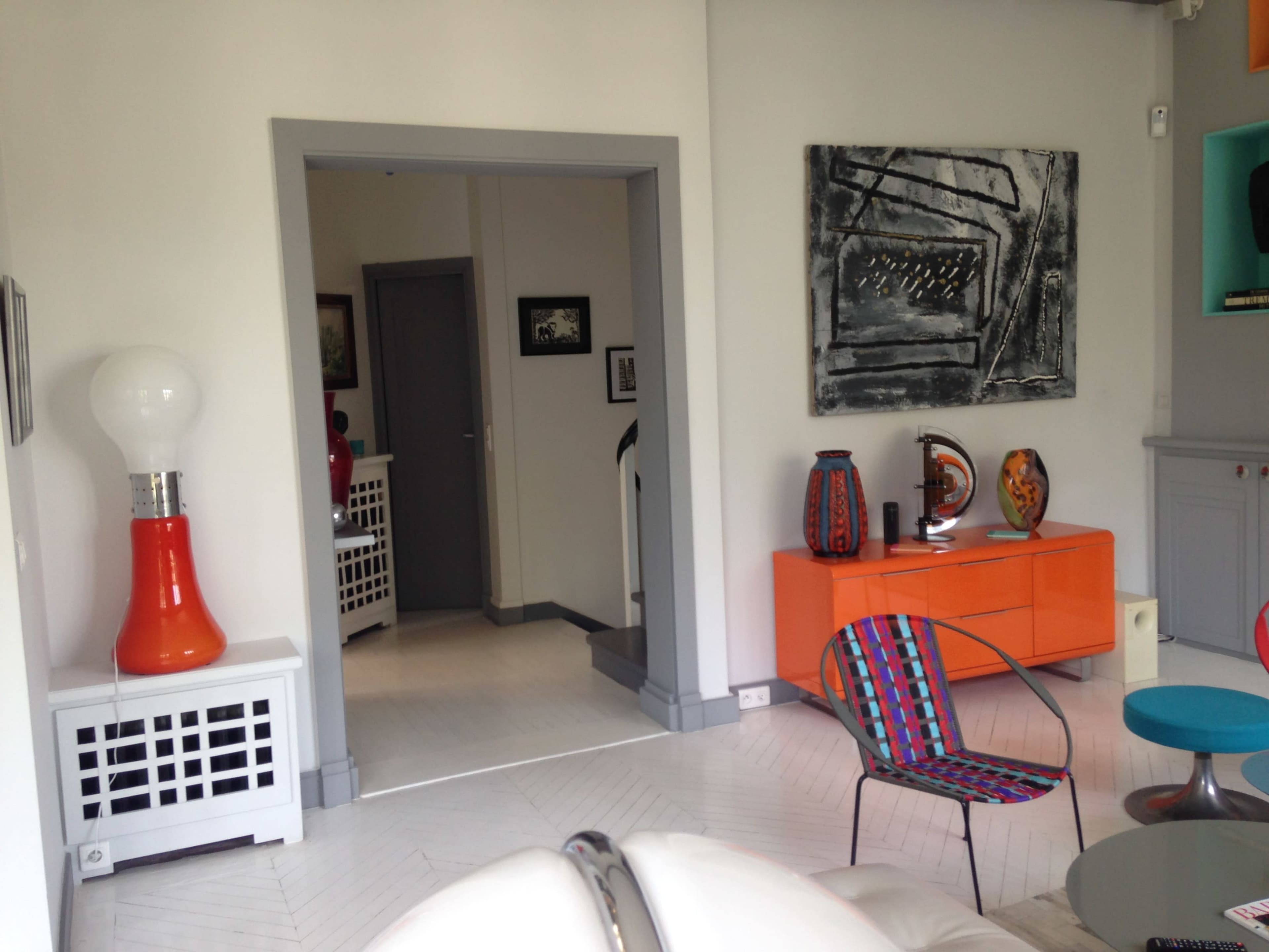 A modern interior featuring a brightly colored orange cabinet, artistic wall decor, and an eclectic mix of furniture.
