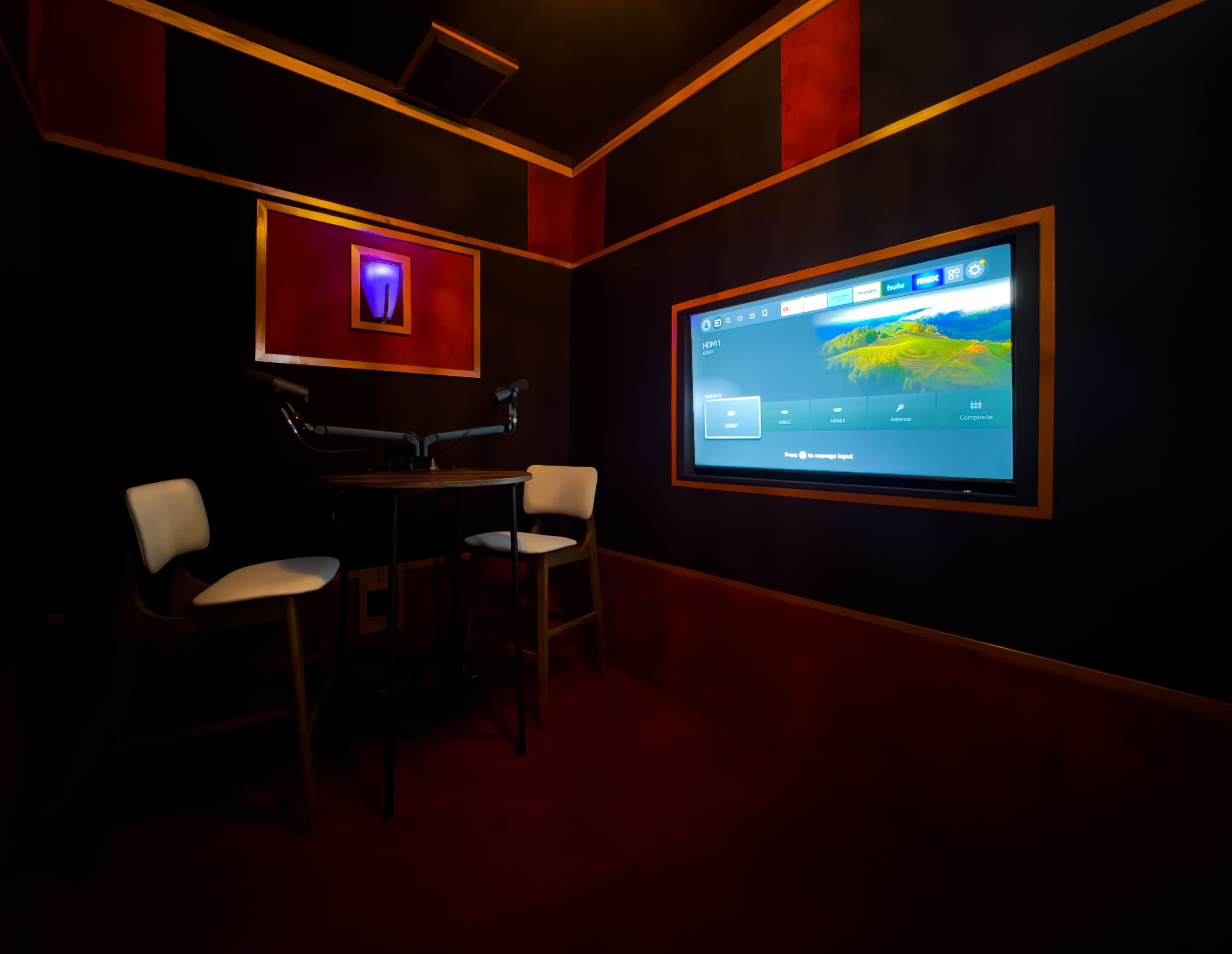 A small room furnished with two white chairs and a table, featuring a large screen mounted on the wall displaying a user interface.